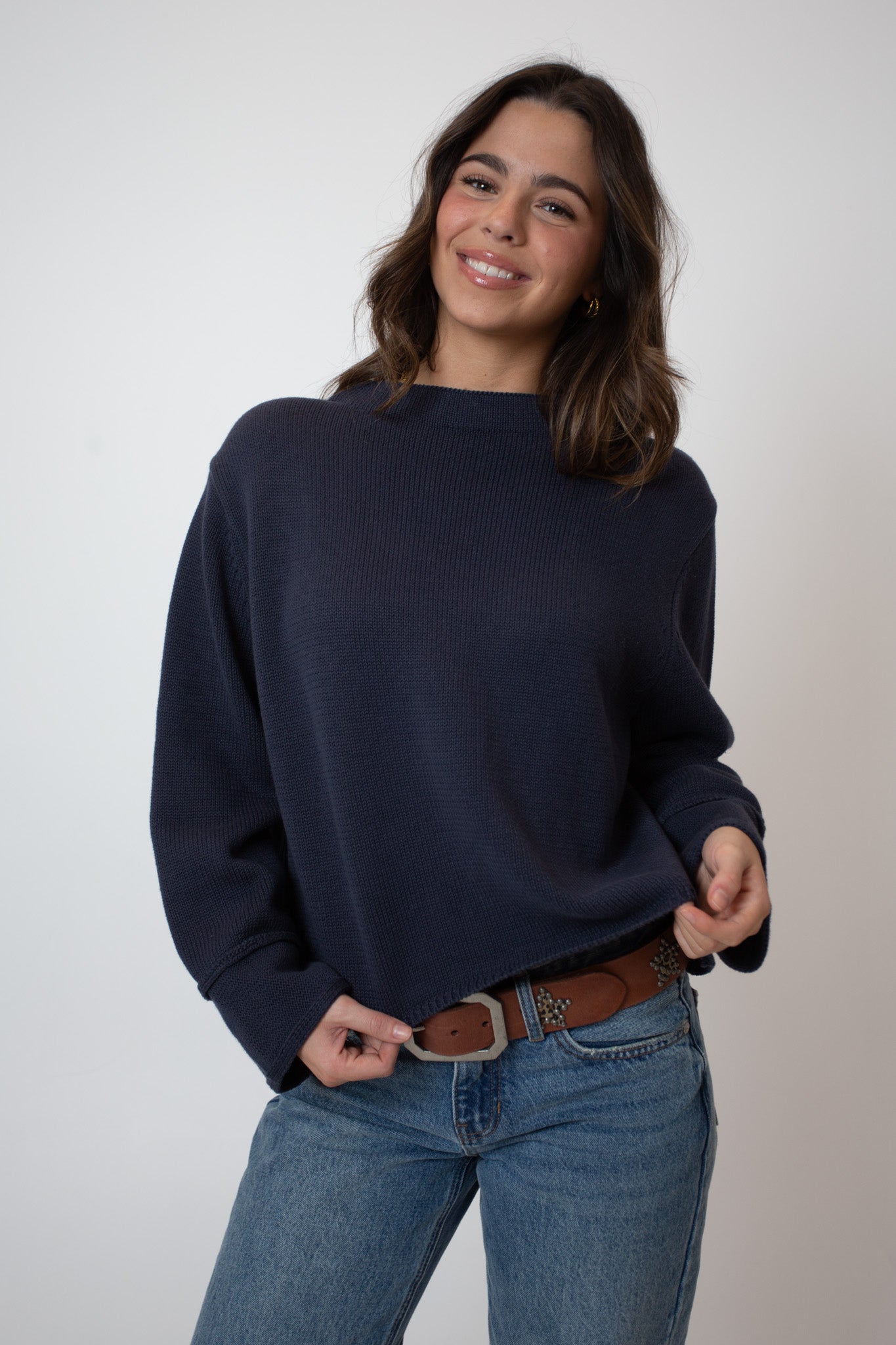 Woman wearing a navy sweater and blue jeans against a plain background