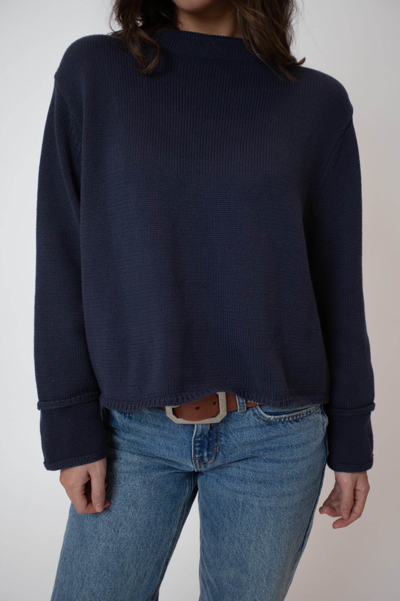 Person wearing a navy sweater and blue jeans on a plain background