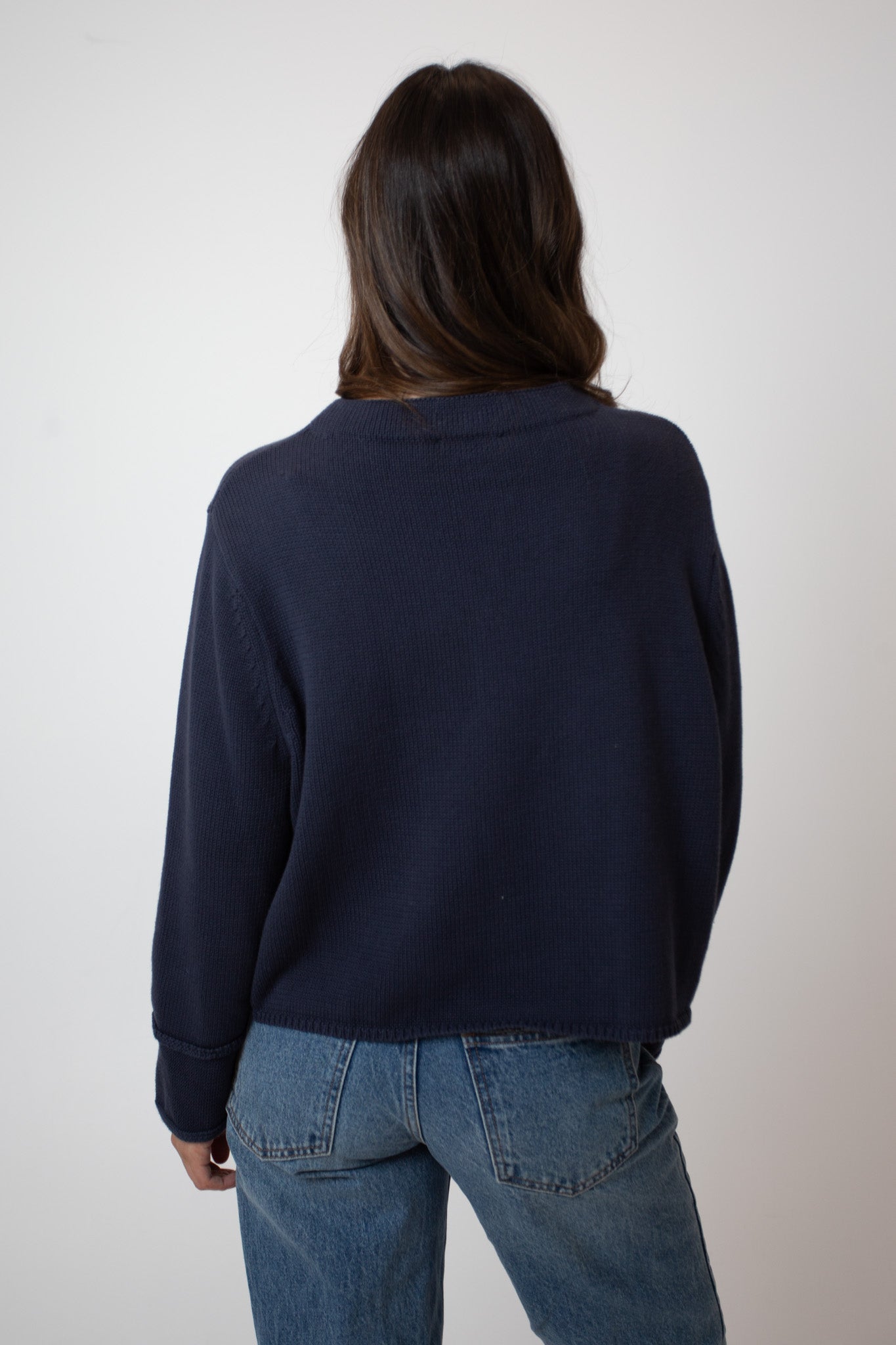 Person wearing a navy sweater and blue jeans against a plain background