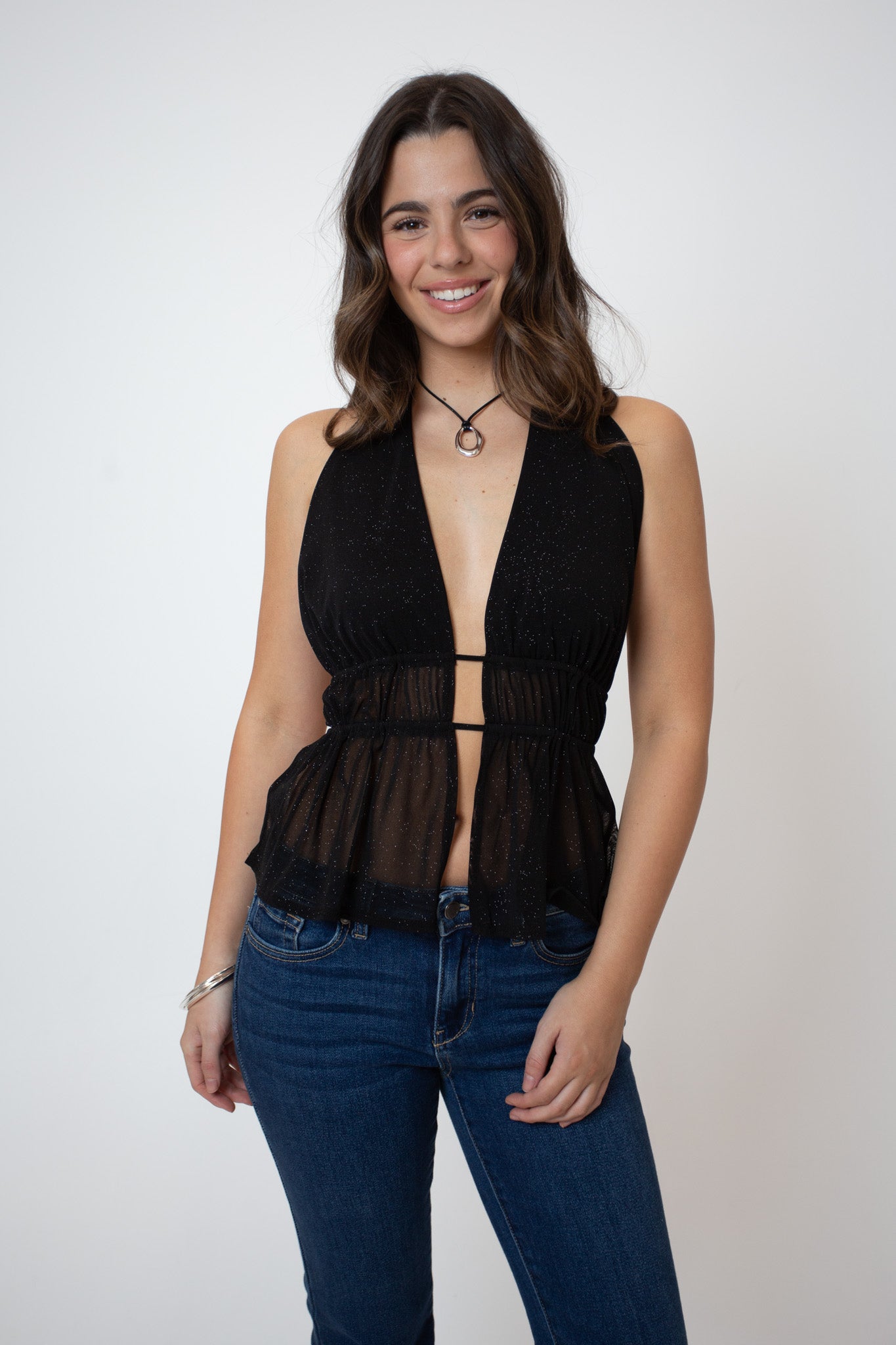 Woman wearing a black sleeveless top with cut-out design and blue jeans on a white background