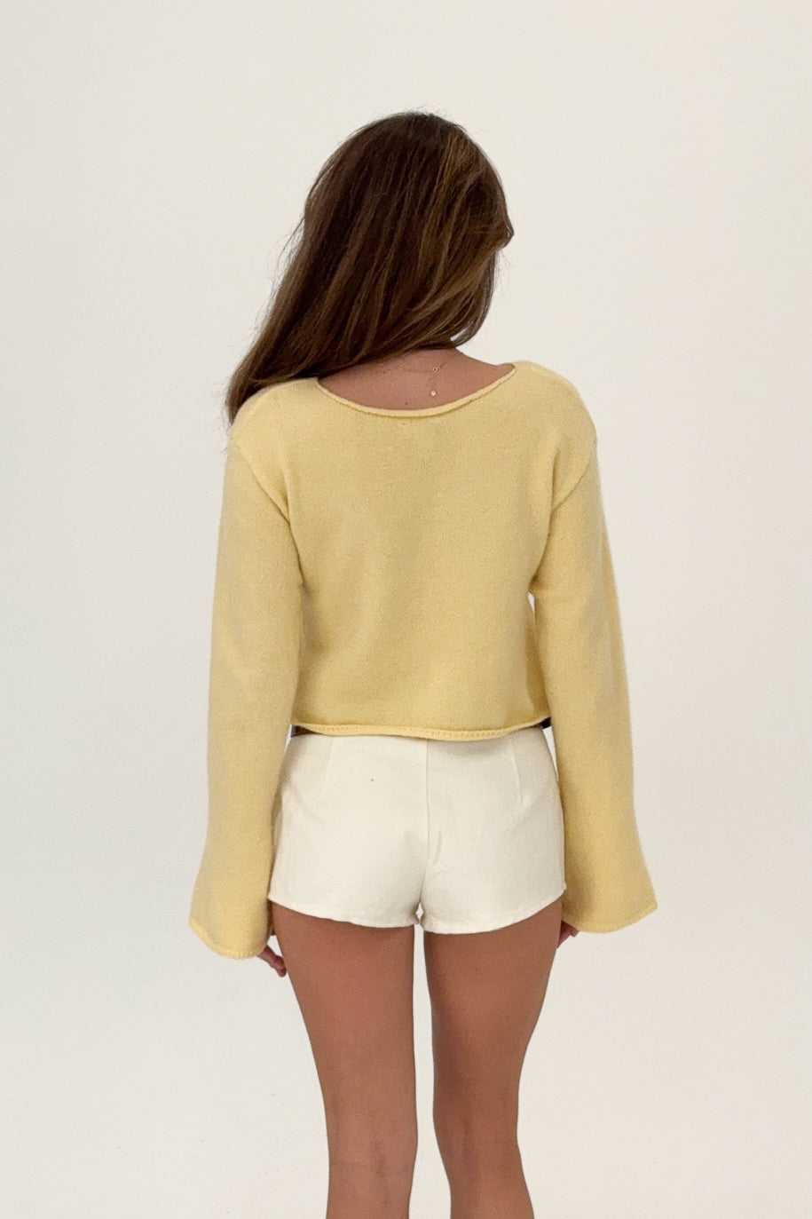 Woman wearing a yellow long-sleeve top and white shorts on a plain background