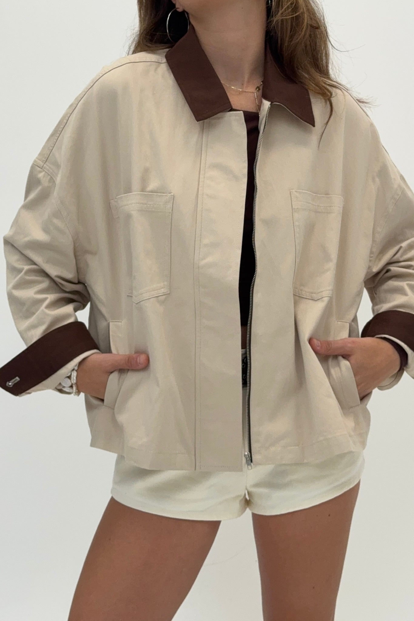 Person wearing a beige jacket with brown collar and cuffs on a white background