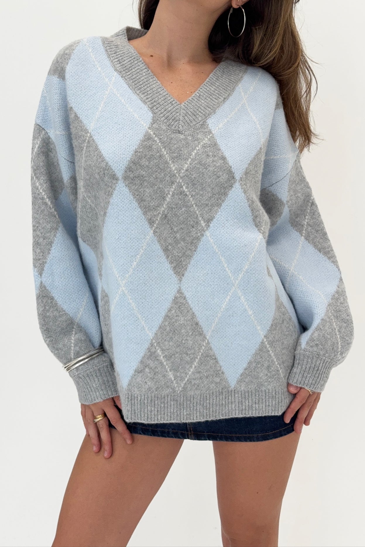 Person wearing a gray and light blue argyle sweater on a white background