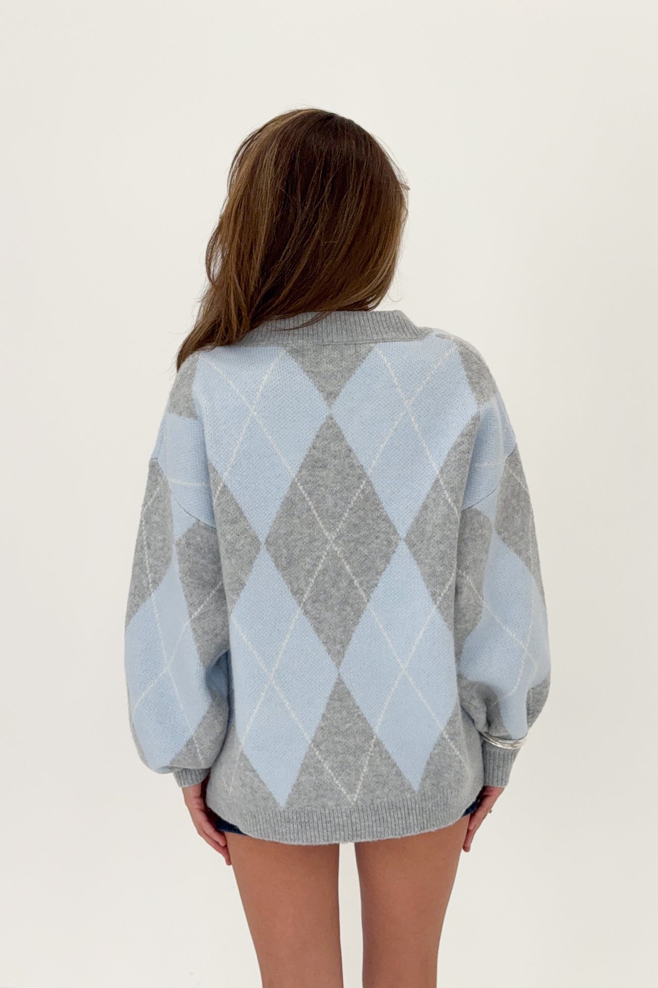 Woman wearing a blue and gray argyle sweater on a white background