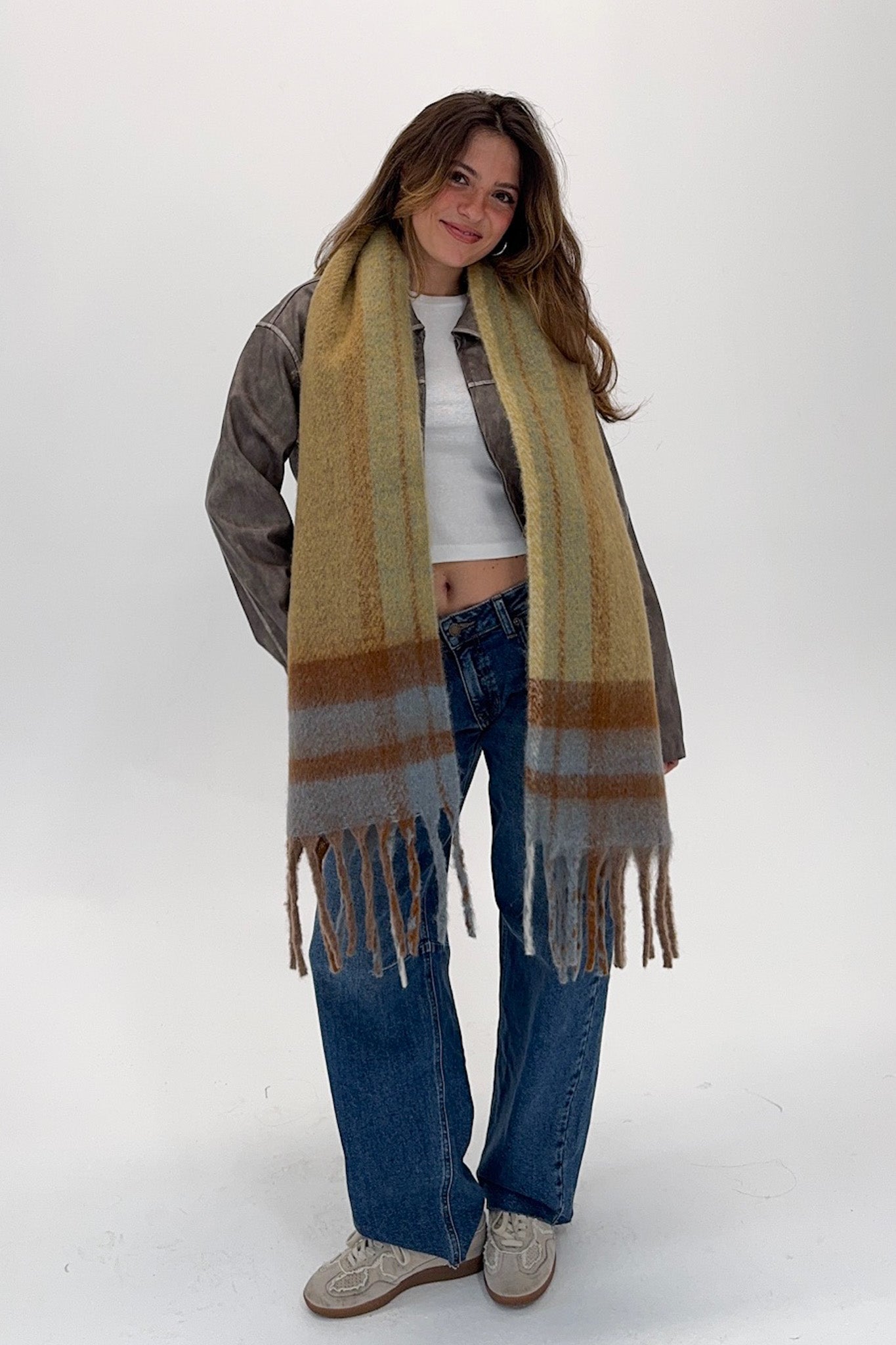 Woman wearing a long plaid scarf, jacket, and jeans on a white background