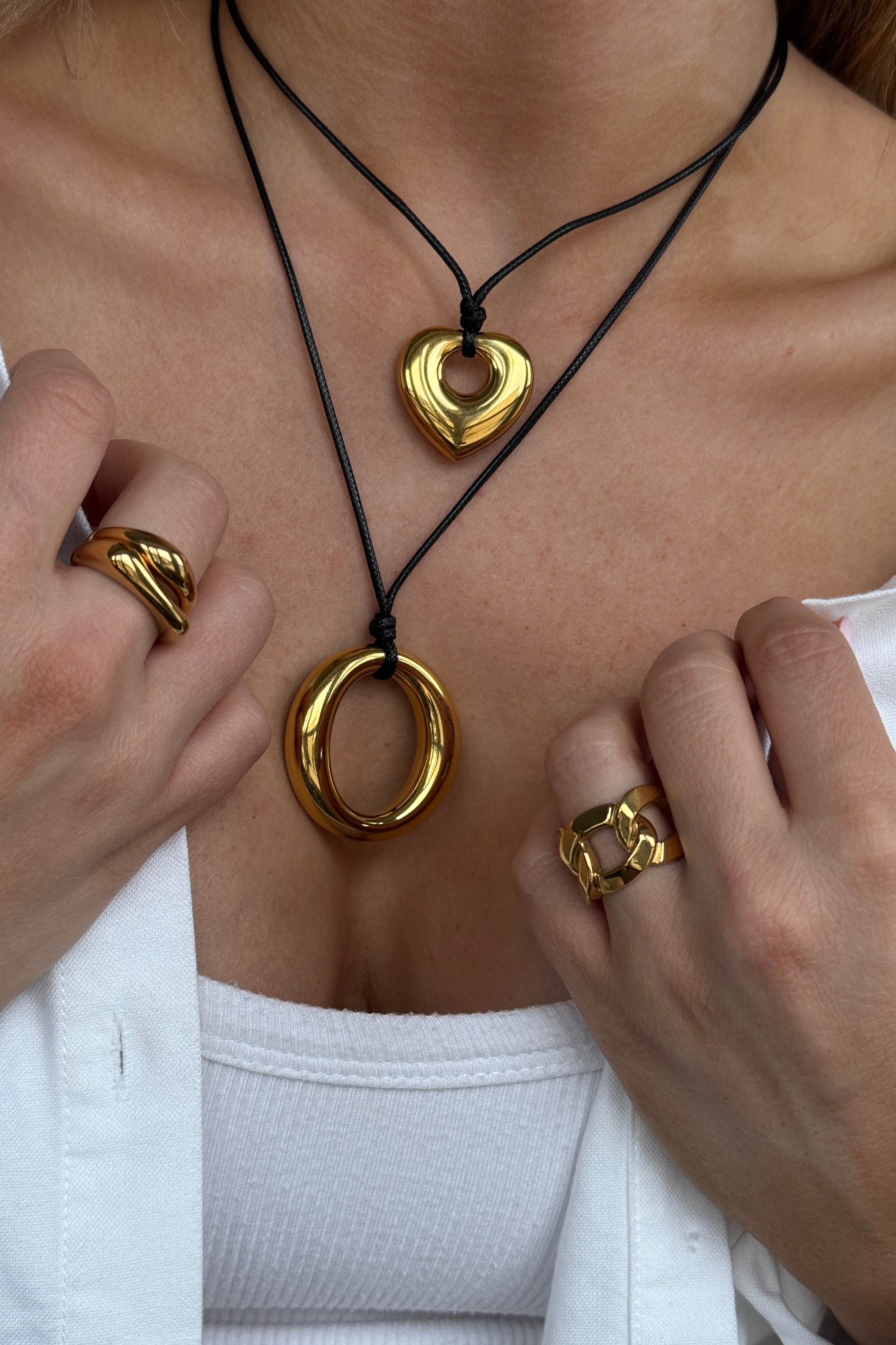 Close-up of a person wearing gold necklaces and rings on a white background