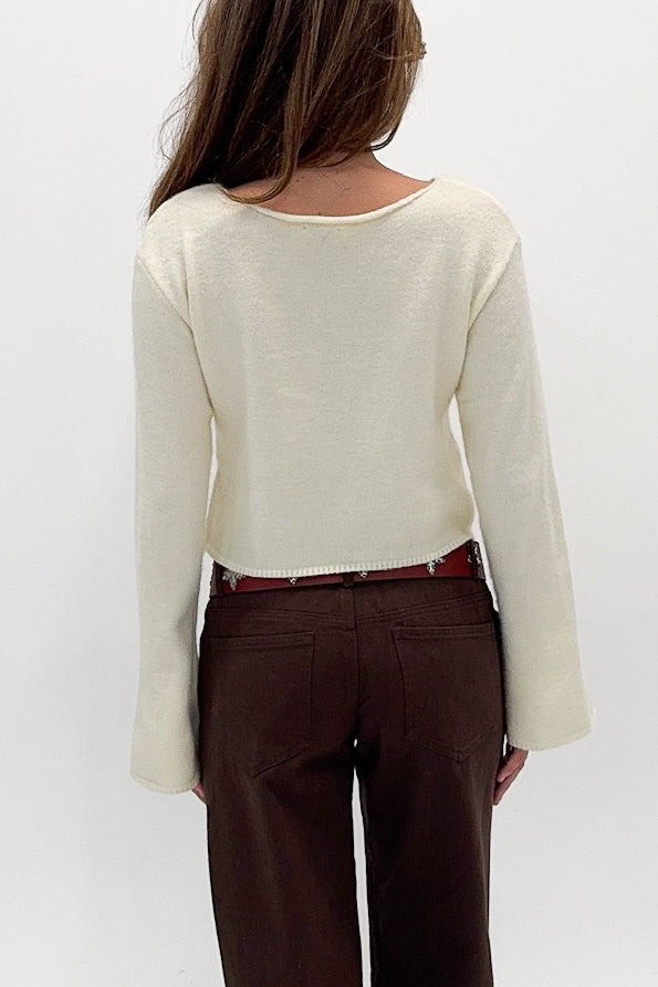 Person wearing a beige sweater and brown pants on a white background