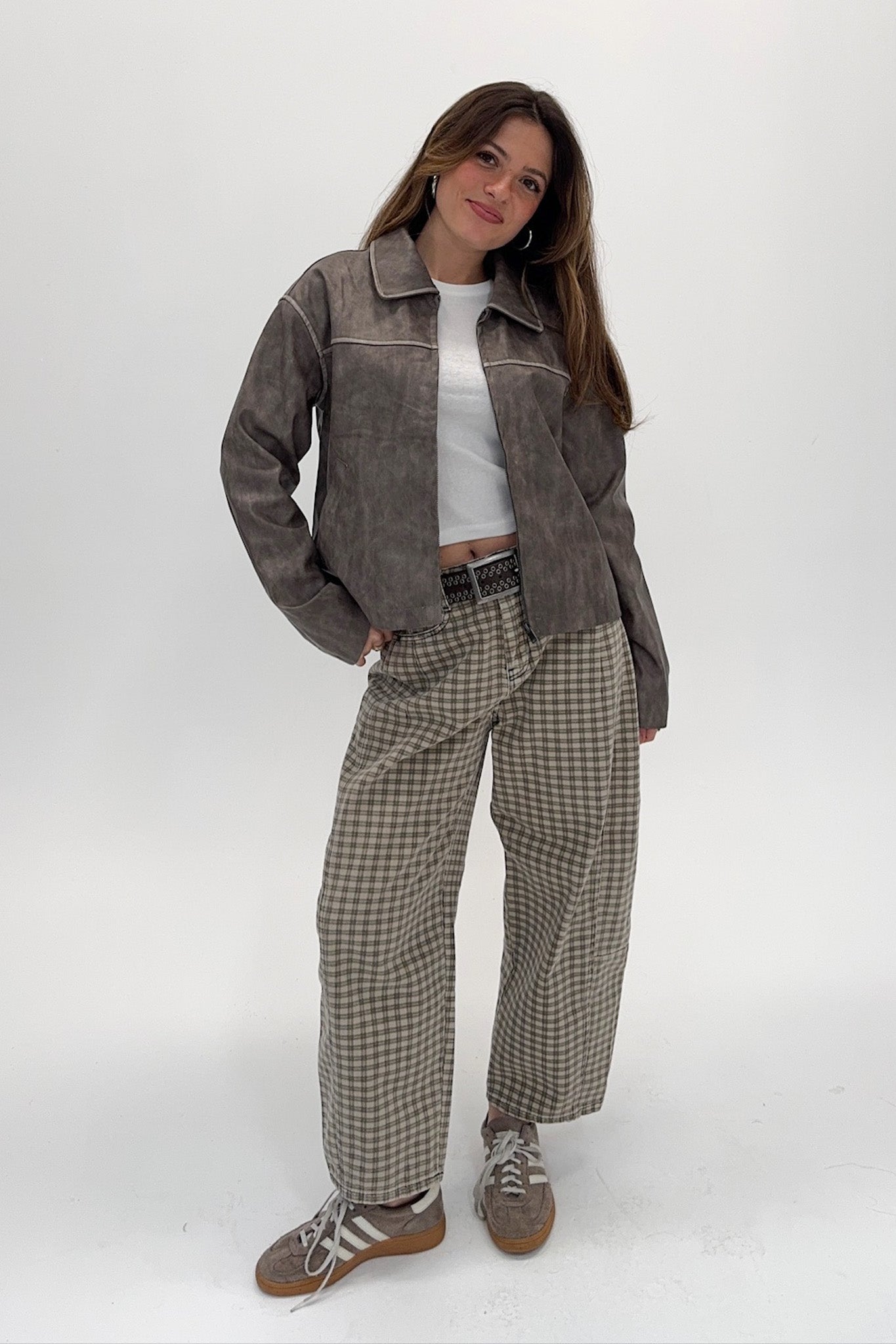 Woman wearing a brown suede jacket and plaid pants on a white background