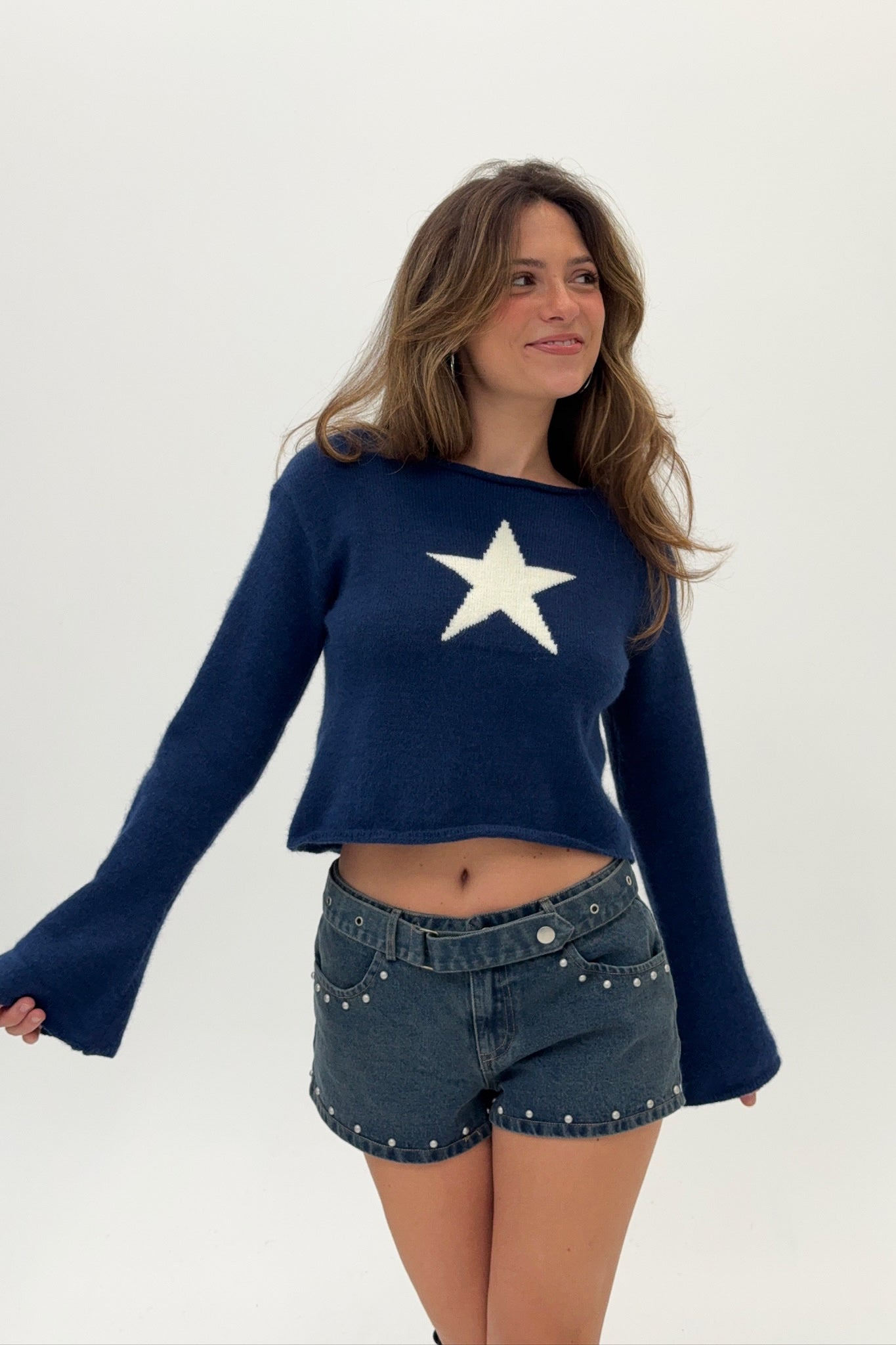 Woman wearing a navy blue sweater with a white star and denim shorts on a white background