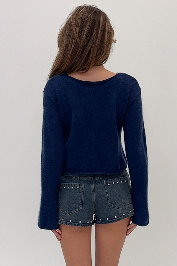 Person wearing a navy blue long-sleeve top and denim shorts with studs on a plain background
