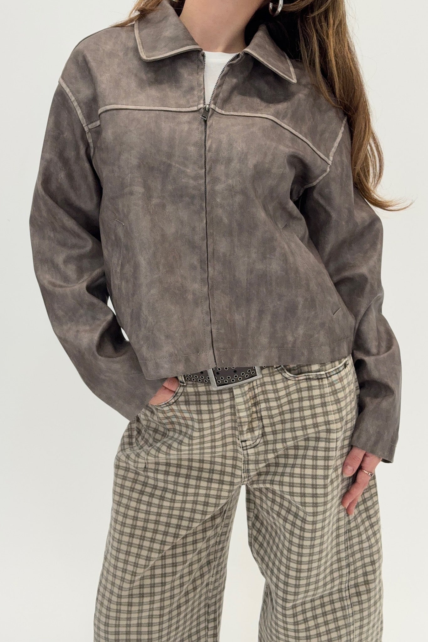 Person wearing a brown jacket and plaid pants on a white background