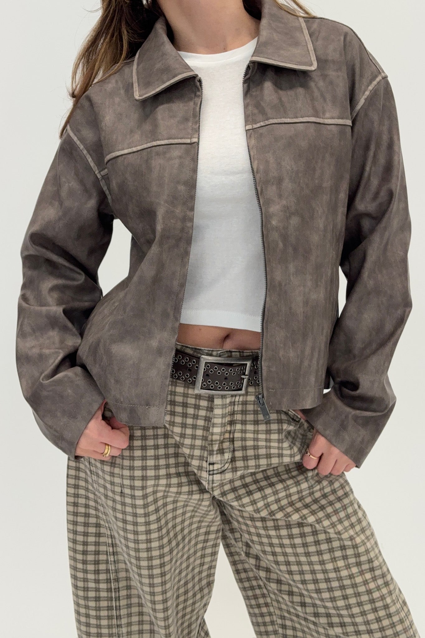 Person wearing a brown suede jacket and plaid pants on a white background