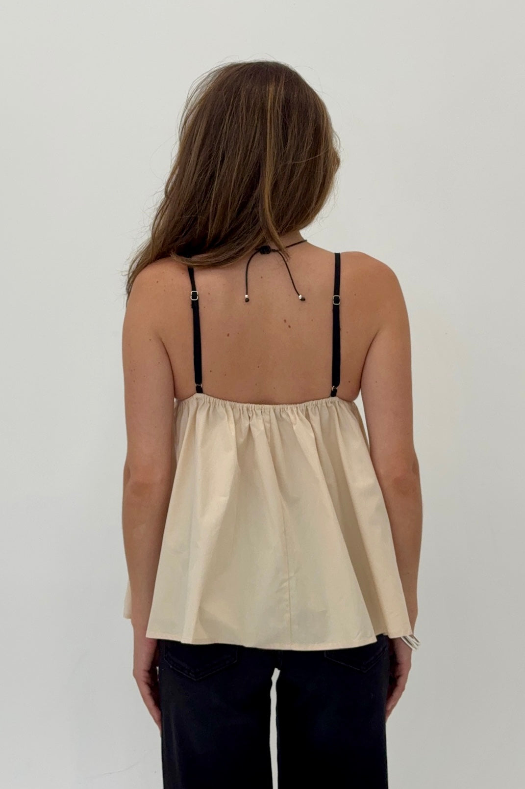 Woman wearing a beige top with thin straps on a plain background