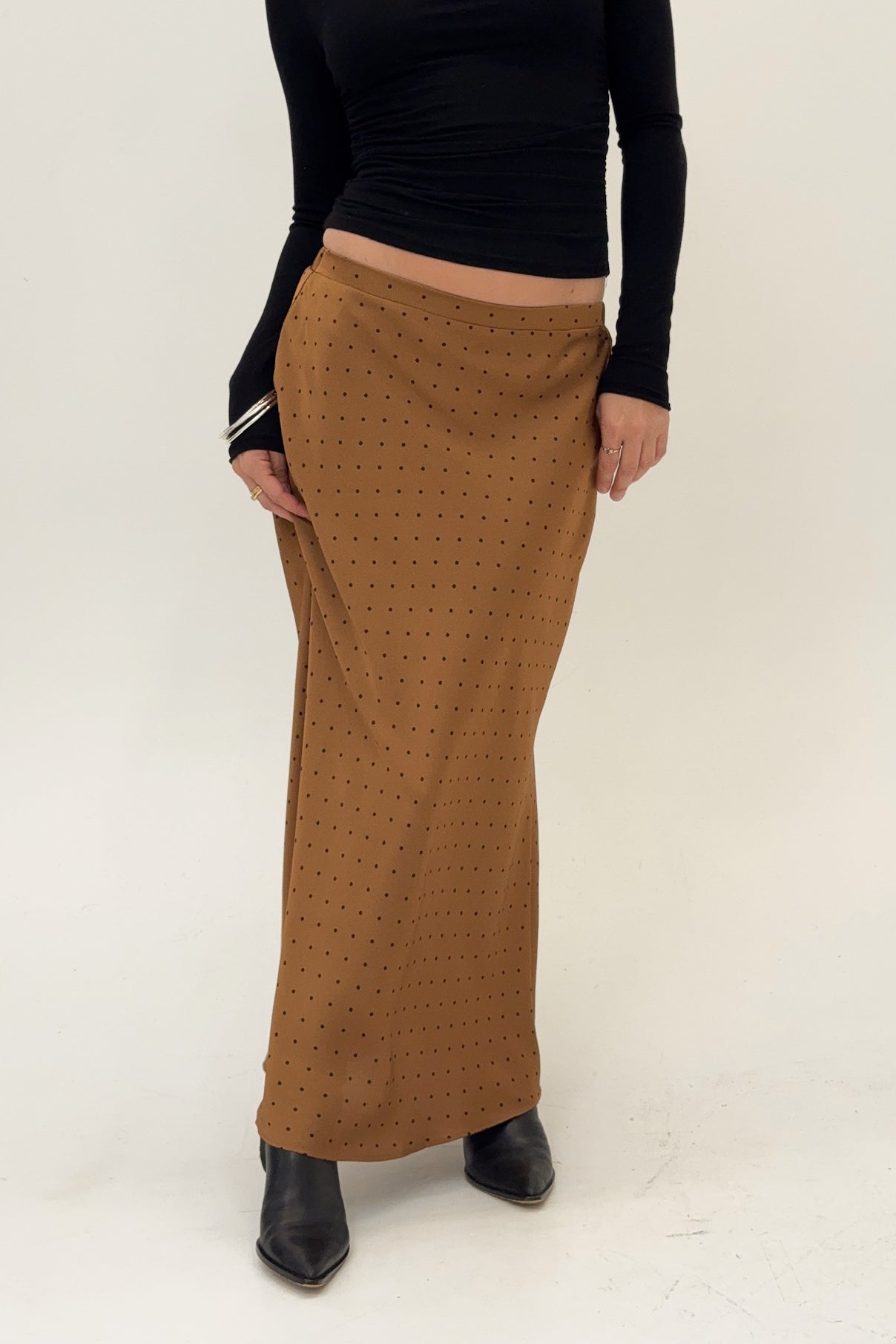 Person wearing a black top and brown patterned skirt on a white background