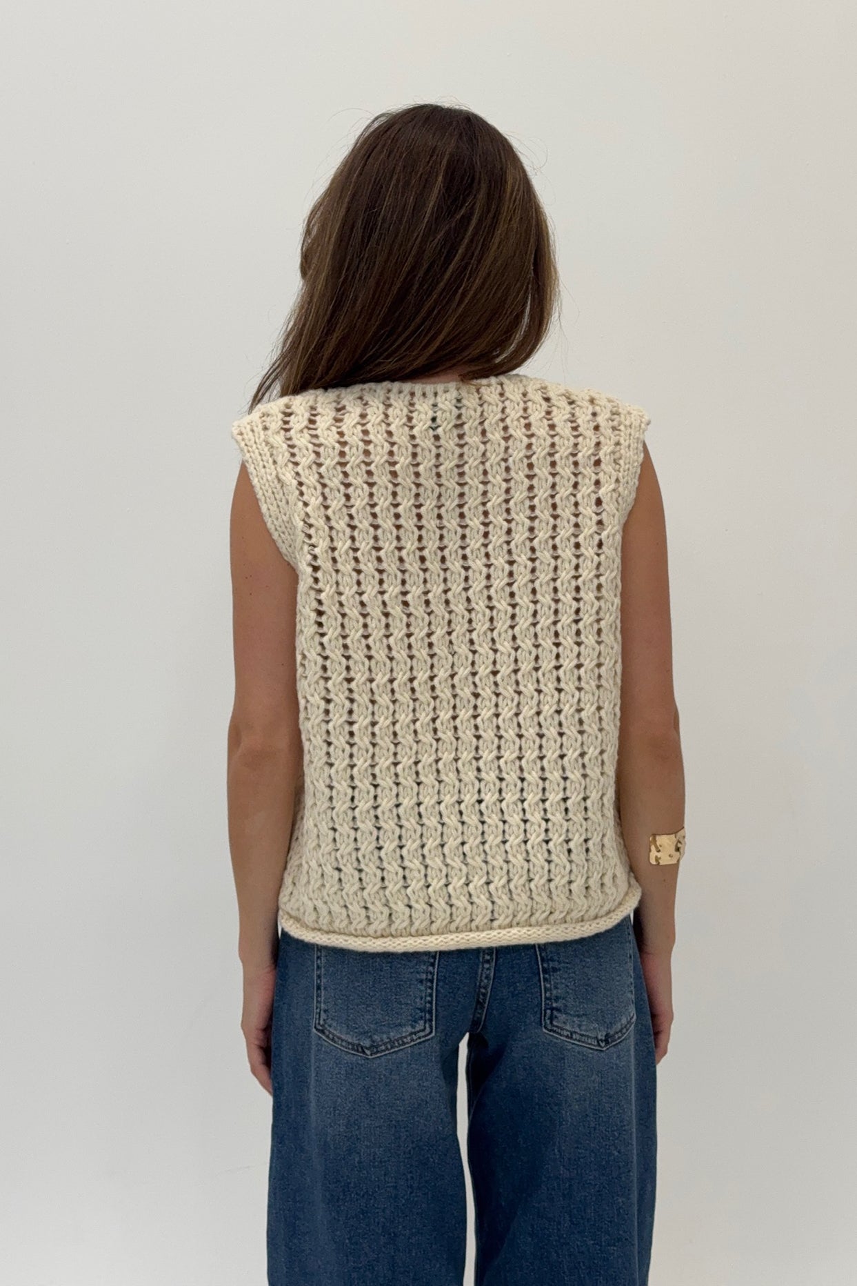 Person wearing a beige knitted vest against a plain background