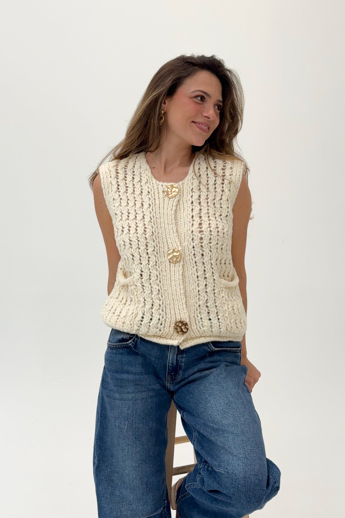 Woman wearing a cream knitted vest and blue jeans on a white background