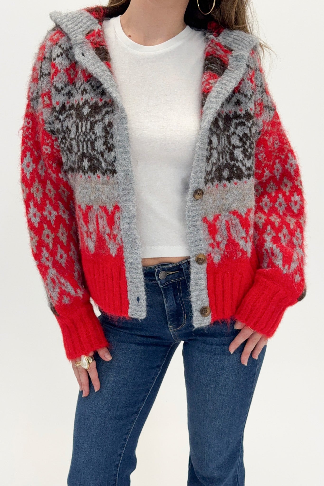 Person wearing a red and gray patterned cardigan over a white shirt and blue jeans.