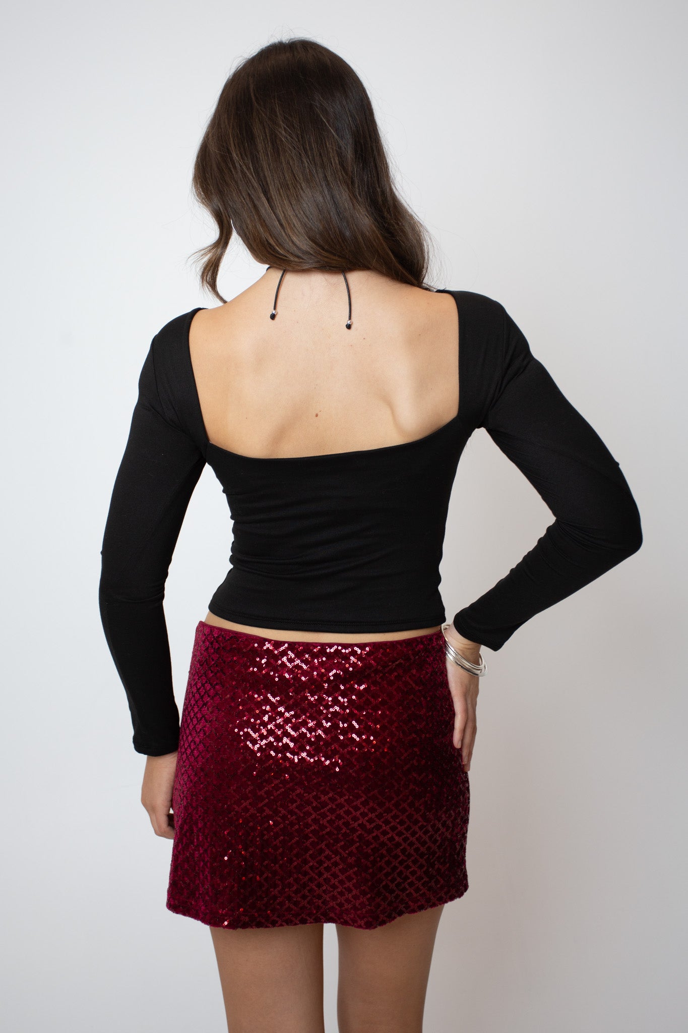 Person wearing a black long-sleeve top and red sequin skirt on a white background