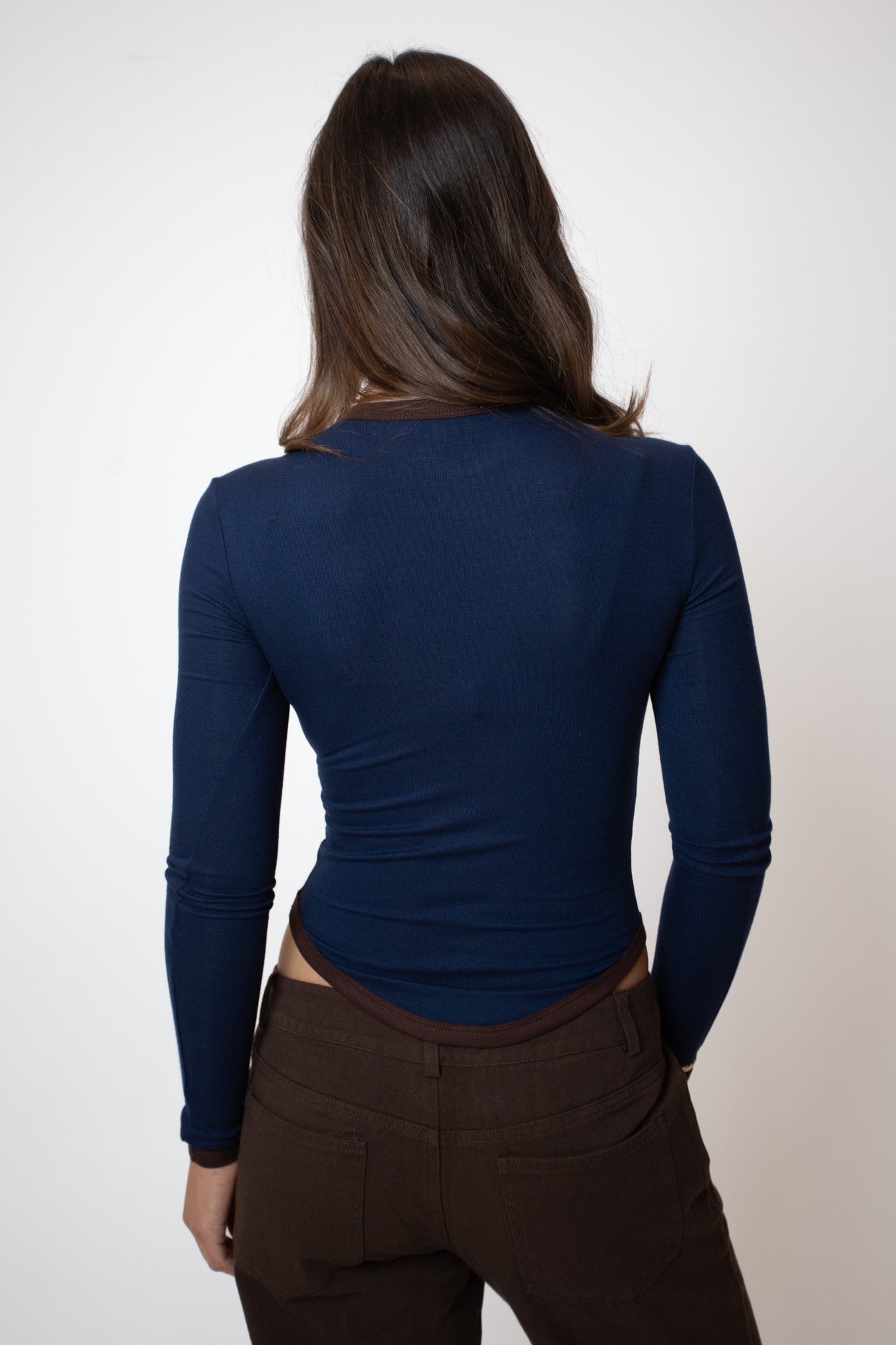 Person wearing a blue long-sleeve top and brown pants on a white background