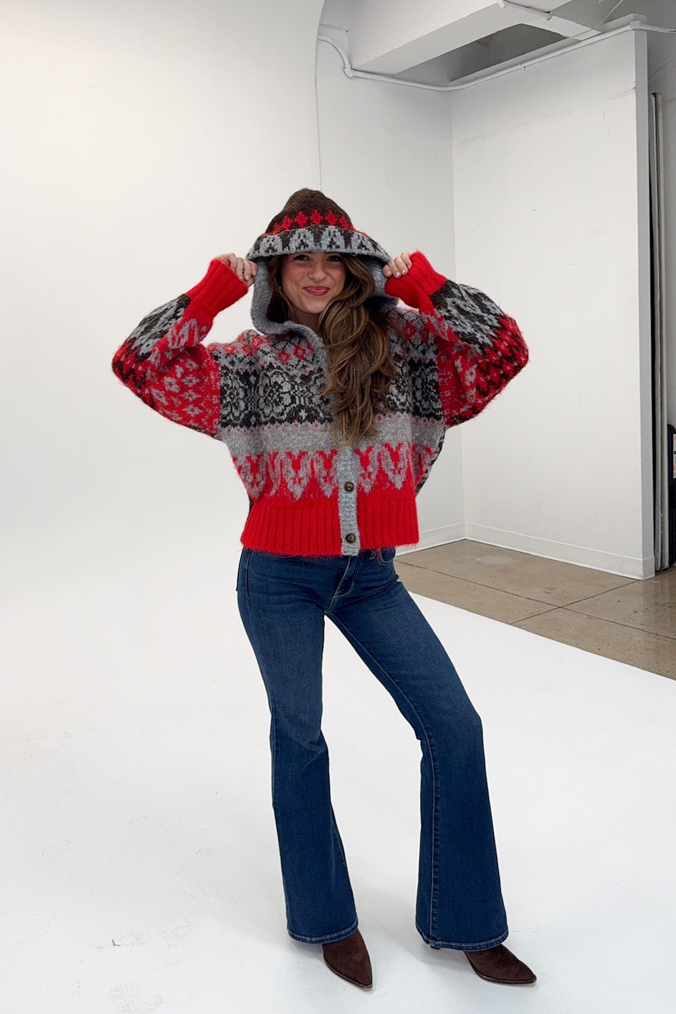 Person wearing a red and gray patterned sweater with a hood in a kitchen.