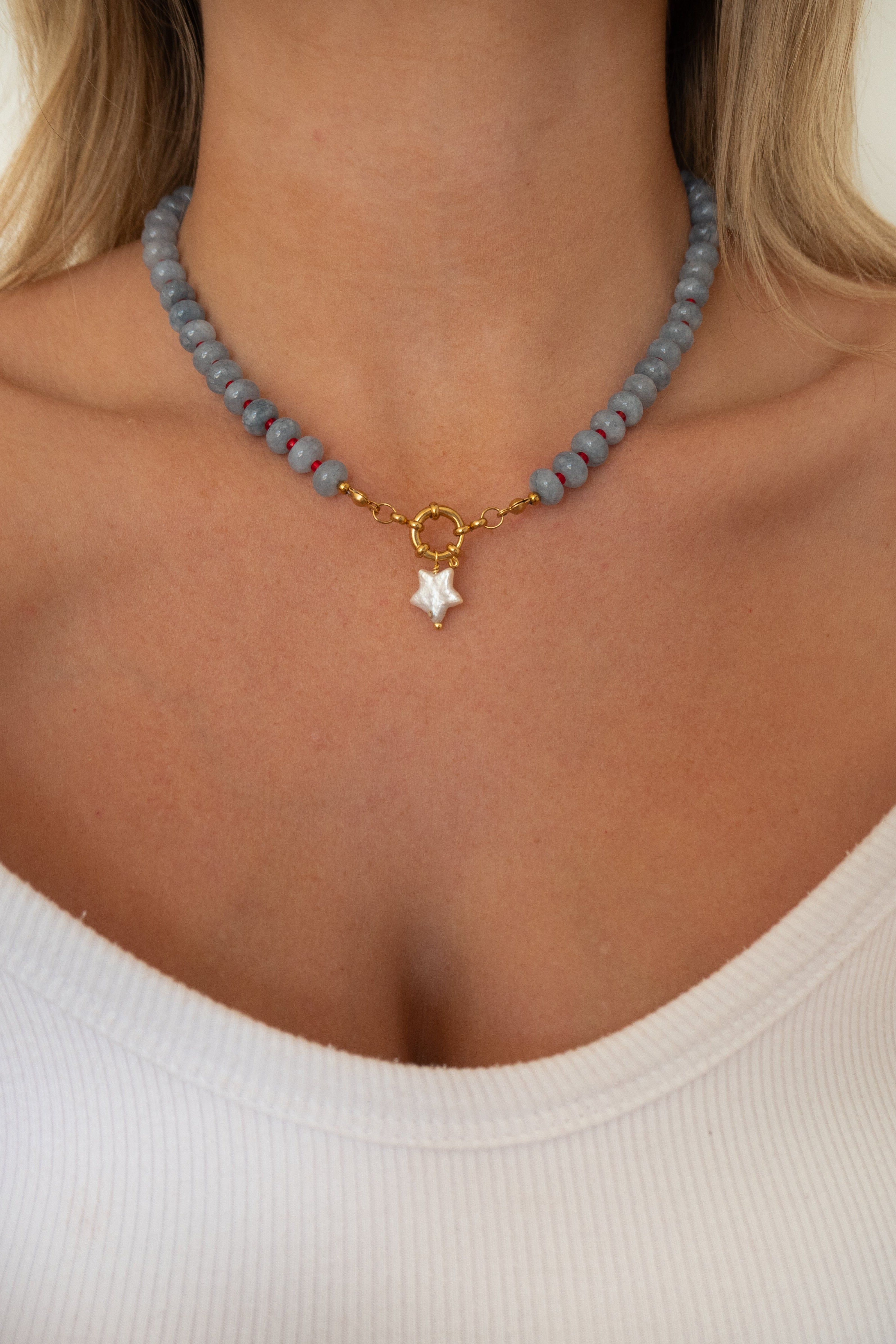 A close-up of a model wearing a light blue beaded choker necklace with a gold ring clasp and a white star charm.