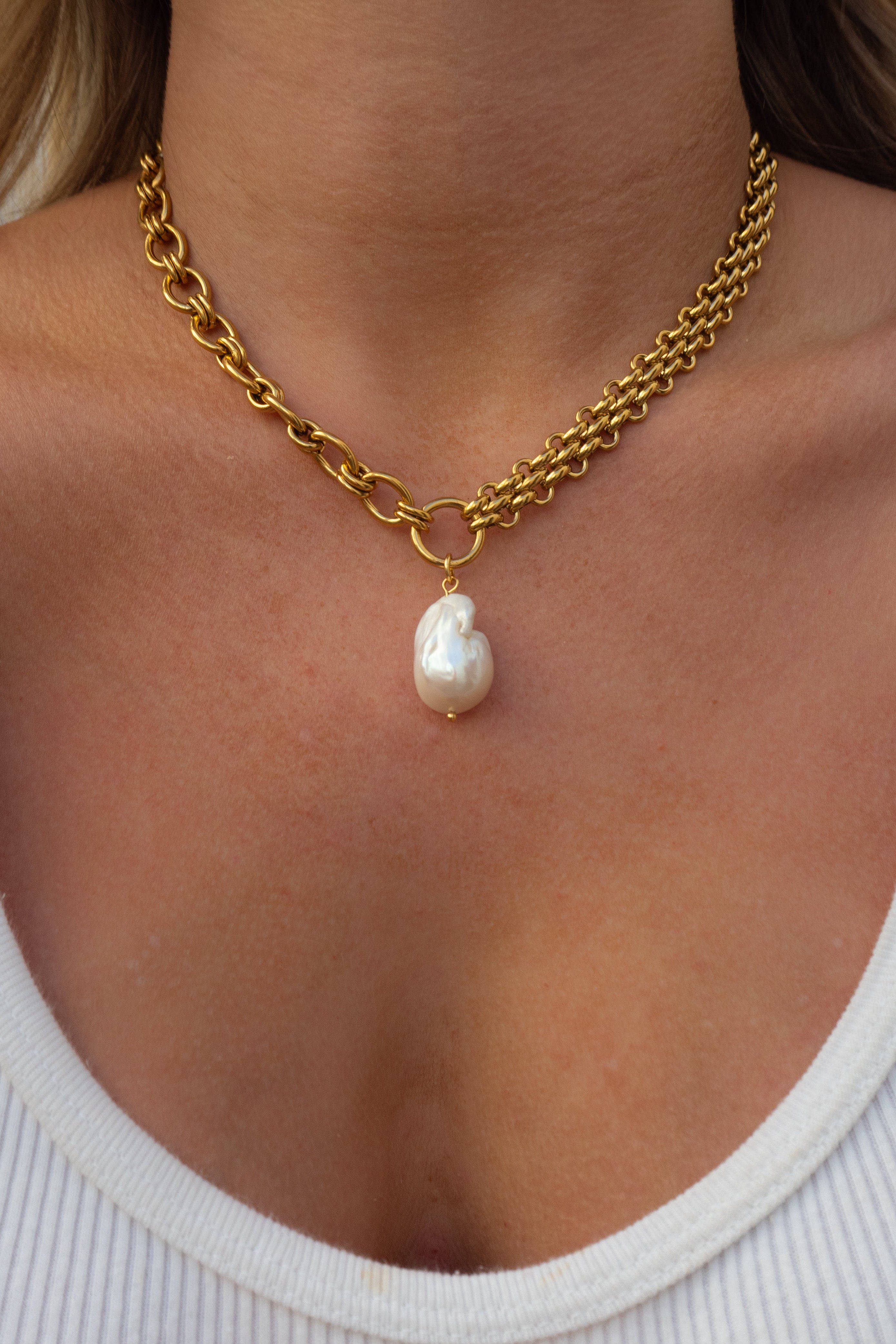 Gold chain necklace with a pearl pendant worn by a person in a white top.