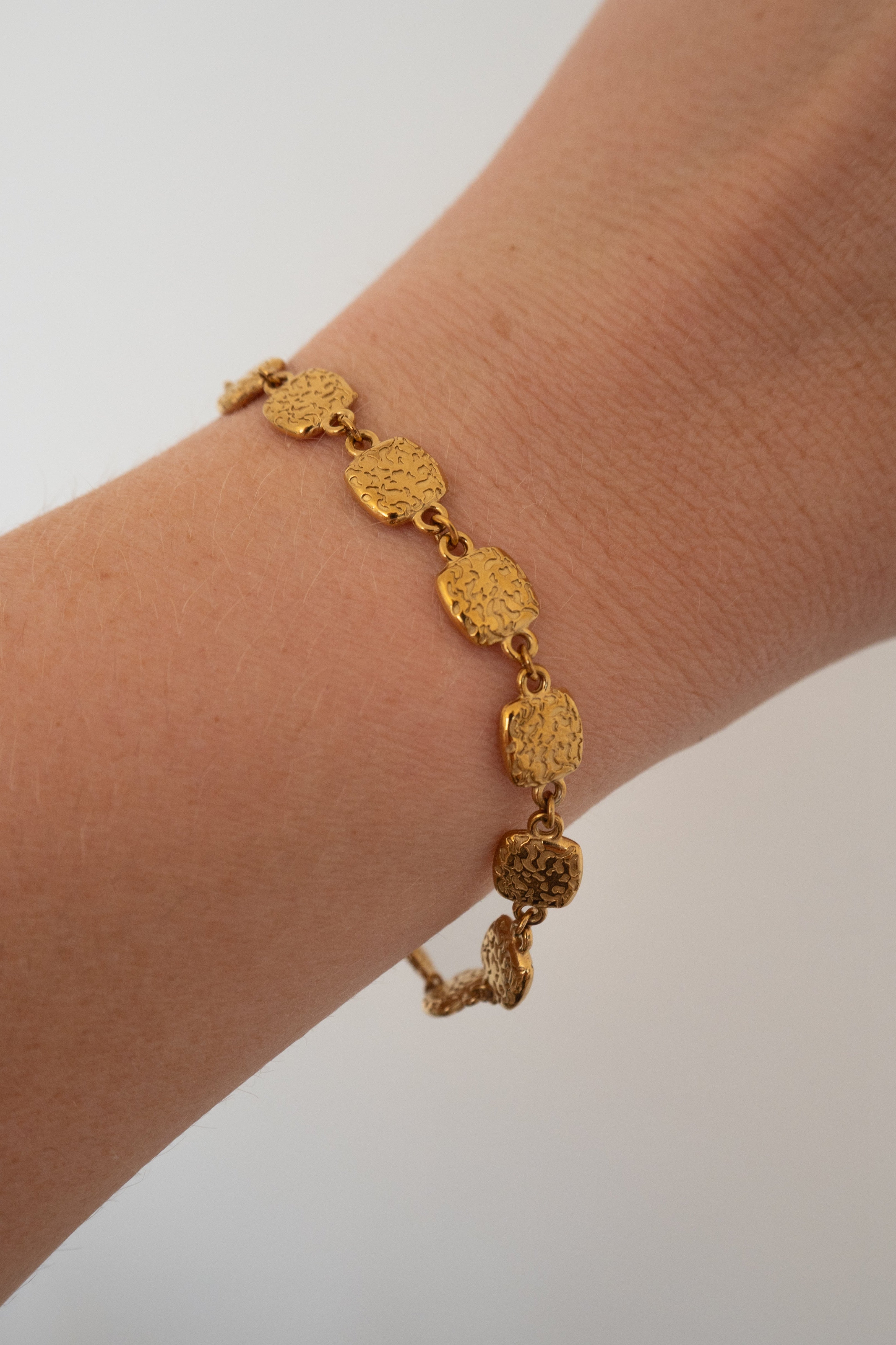 A textured gold link bracelet worn on a person's wrist, shown against a plain light gray background.