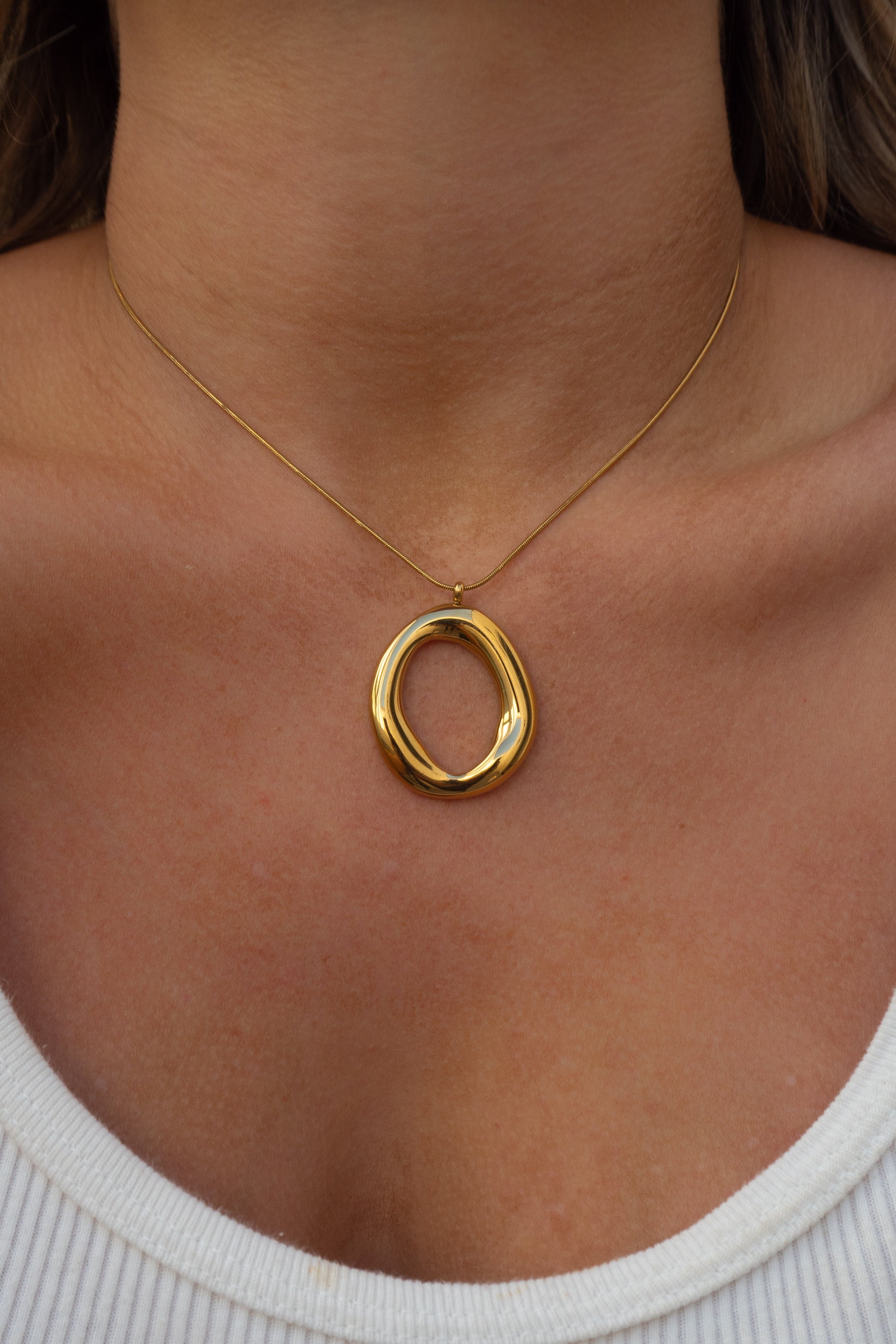 Gold necklace with a circular pendant on a person wearing a white top.