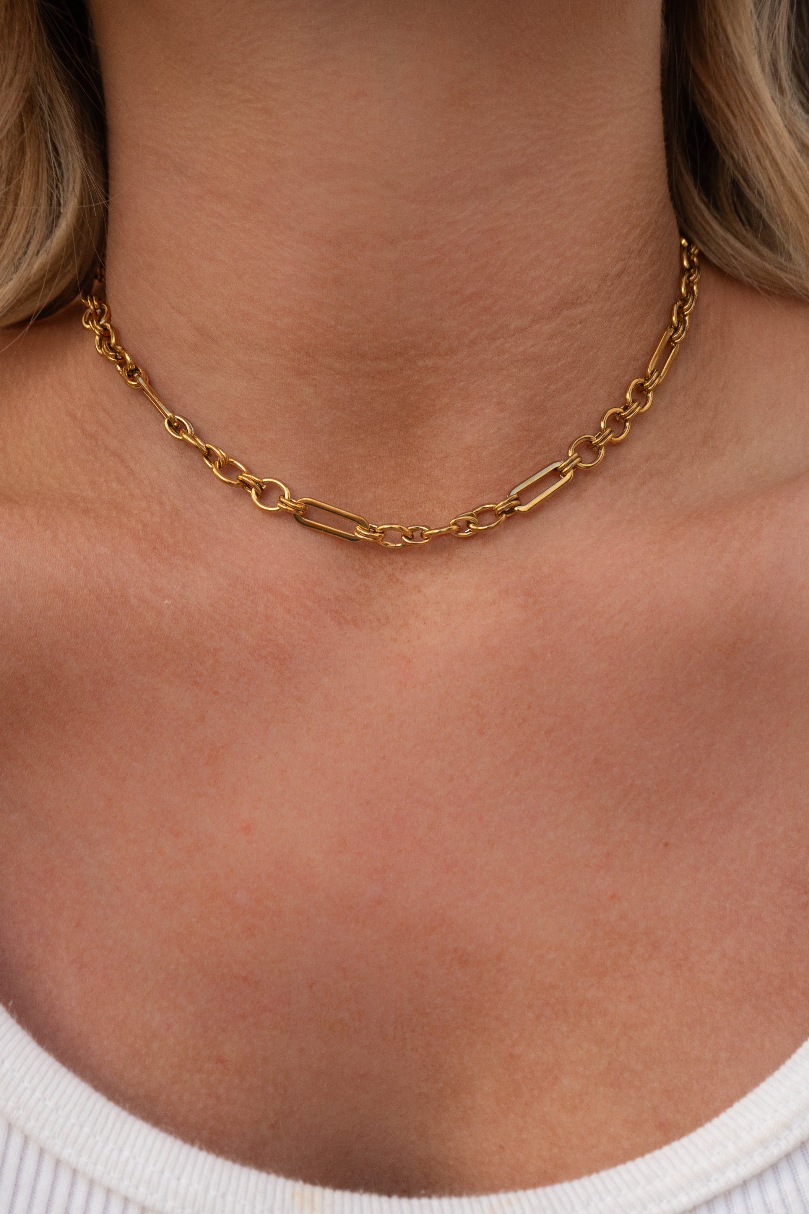 Gold chain necklace on a person wearing a white top