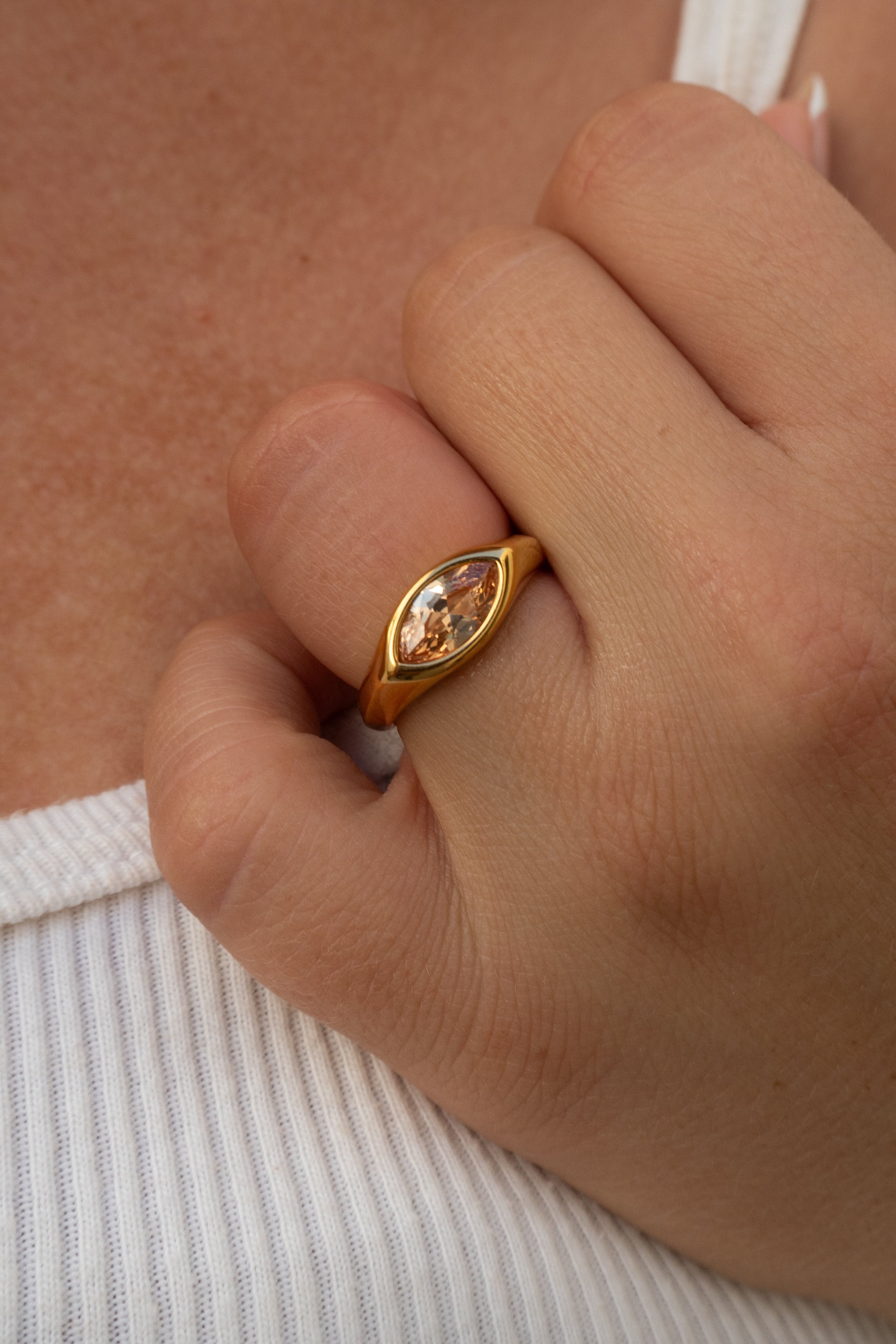 Gold ring with a gemstone on a person's finger against a neutral background