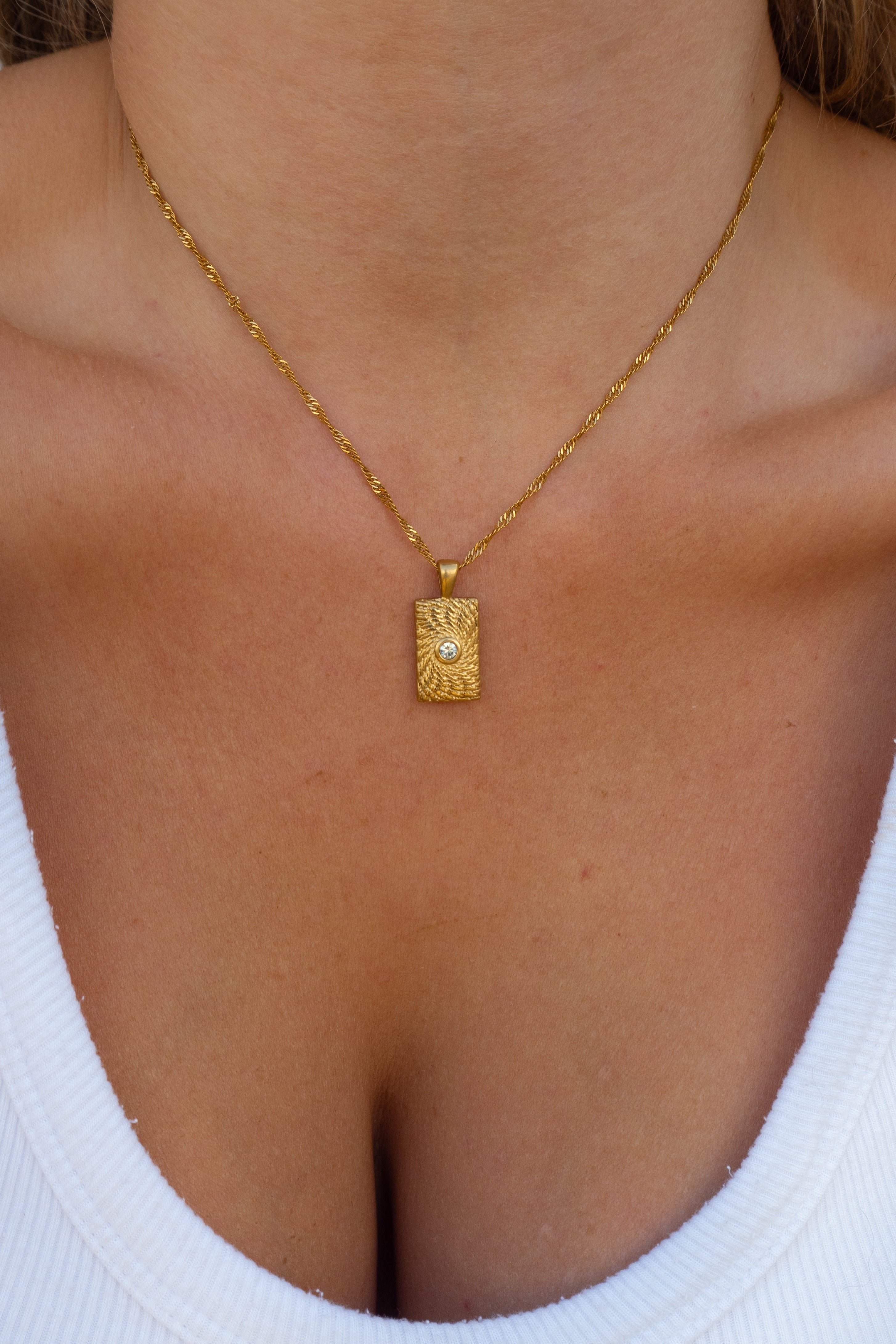 Gold necklace with a pendant on a person wearing a white top