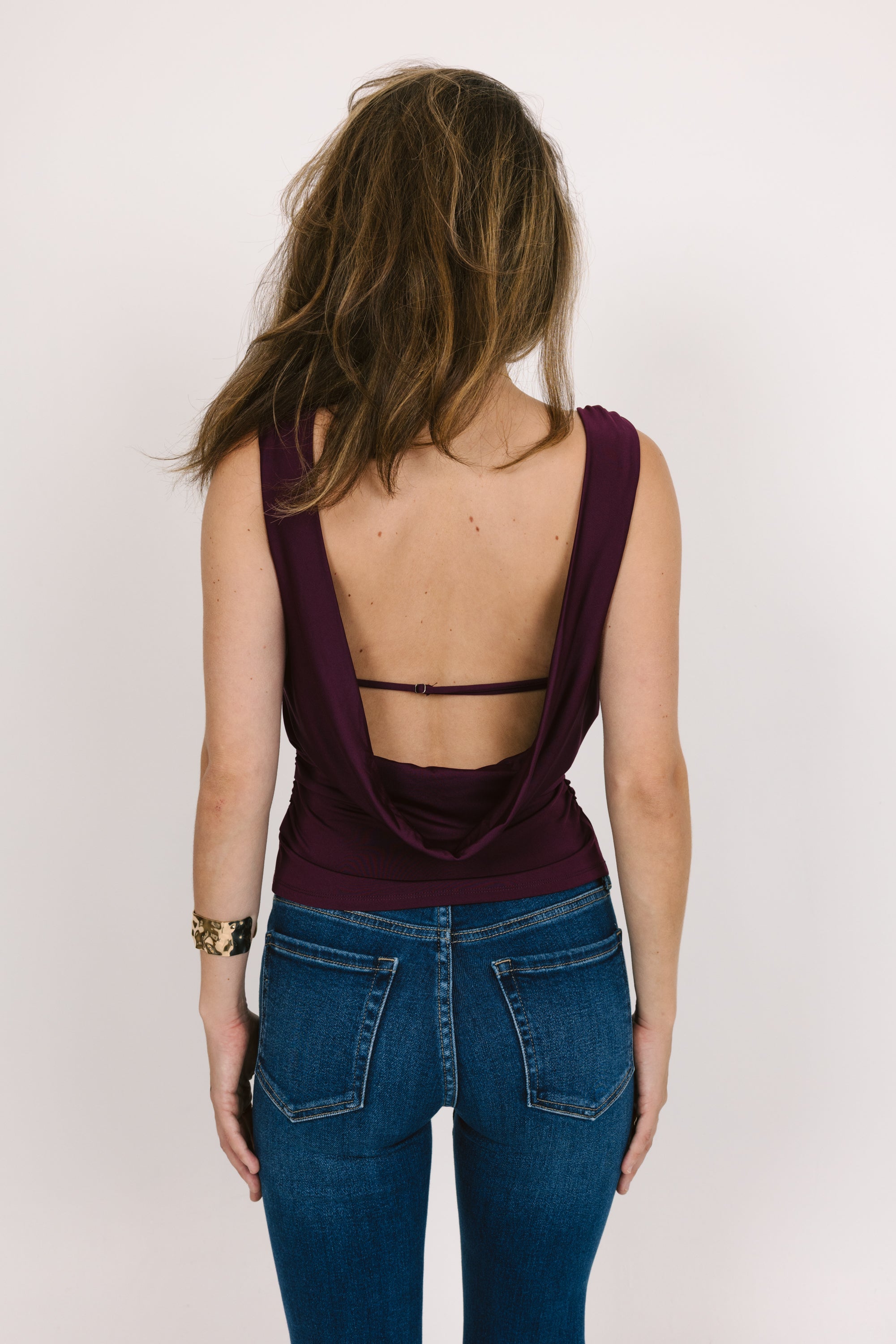 Person wearing a purple open-back top and blue jeans on a white background