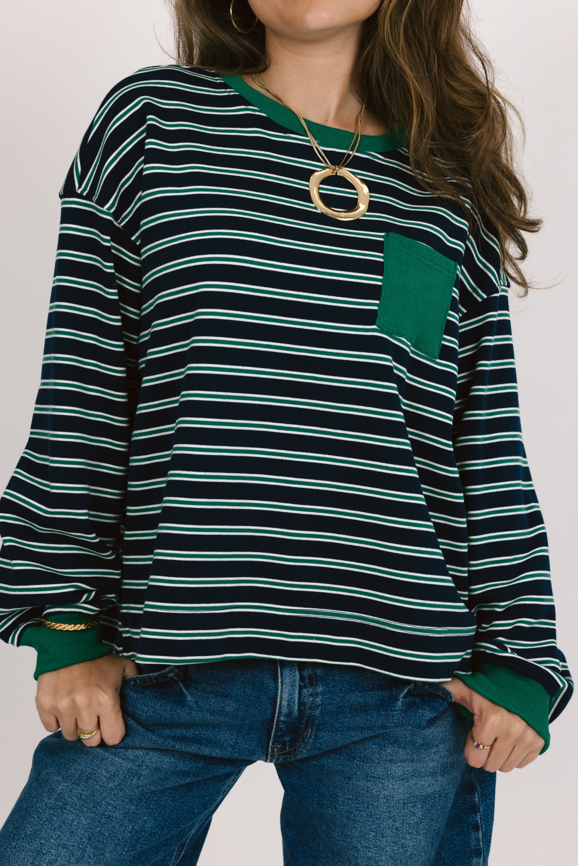 Person wearing a green and black striped sweater with a pocket on a white background