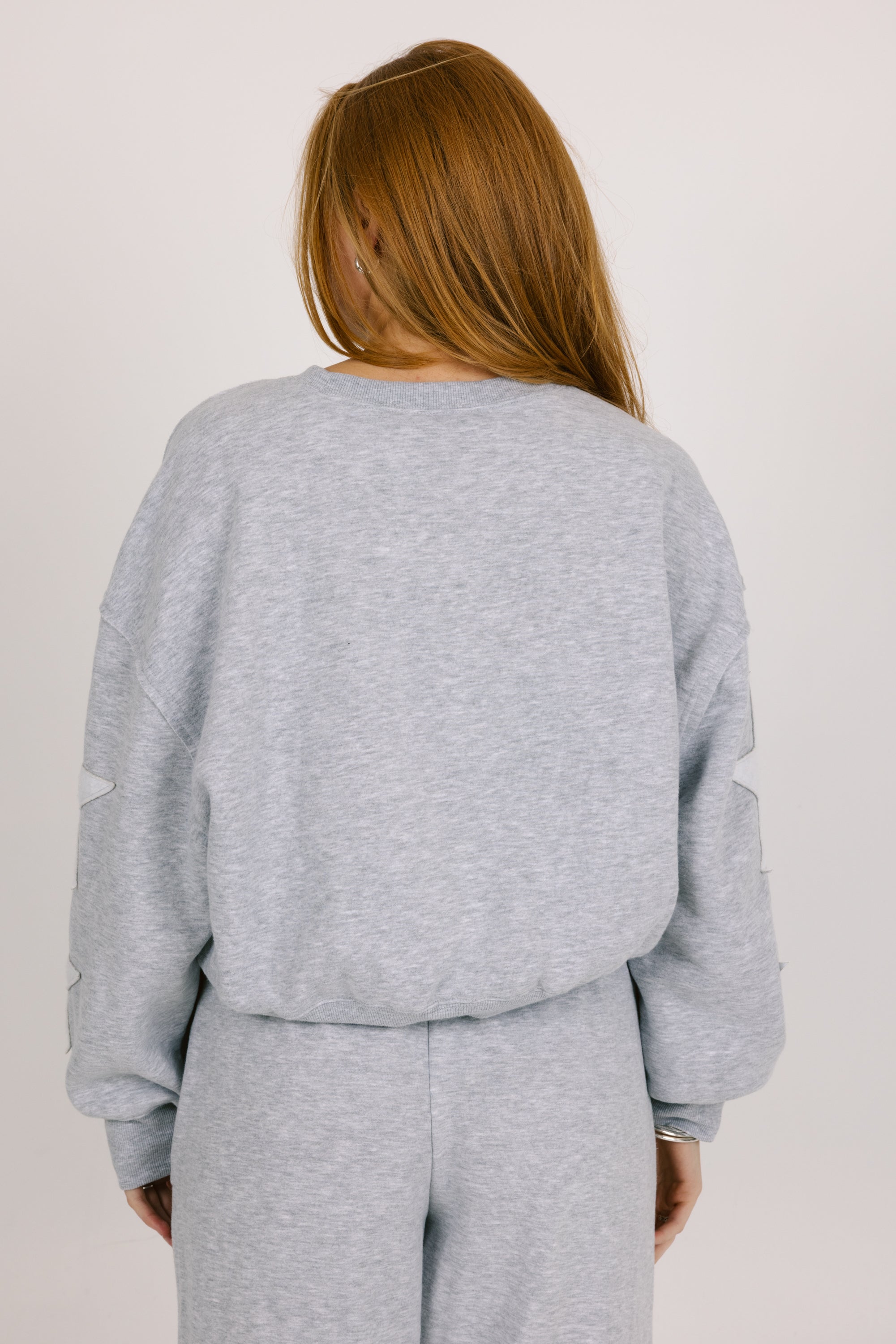 Person wearing a gray sweatshirt and pants set on a plain background