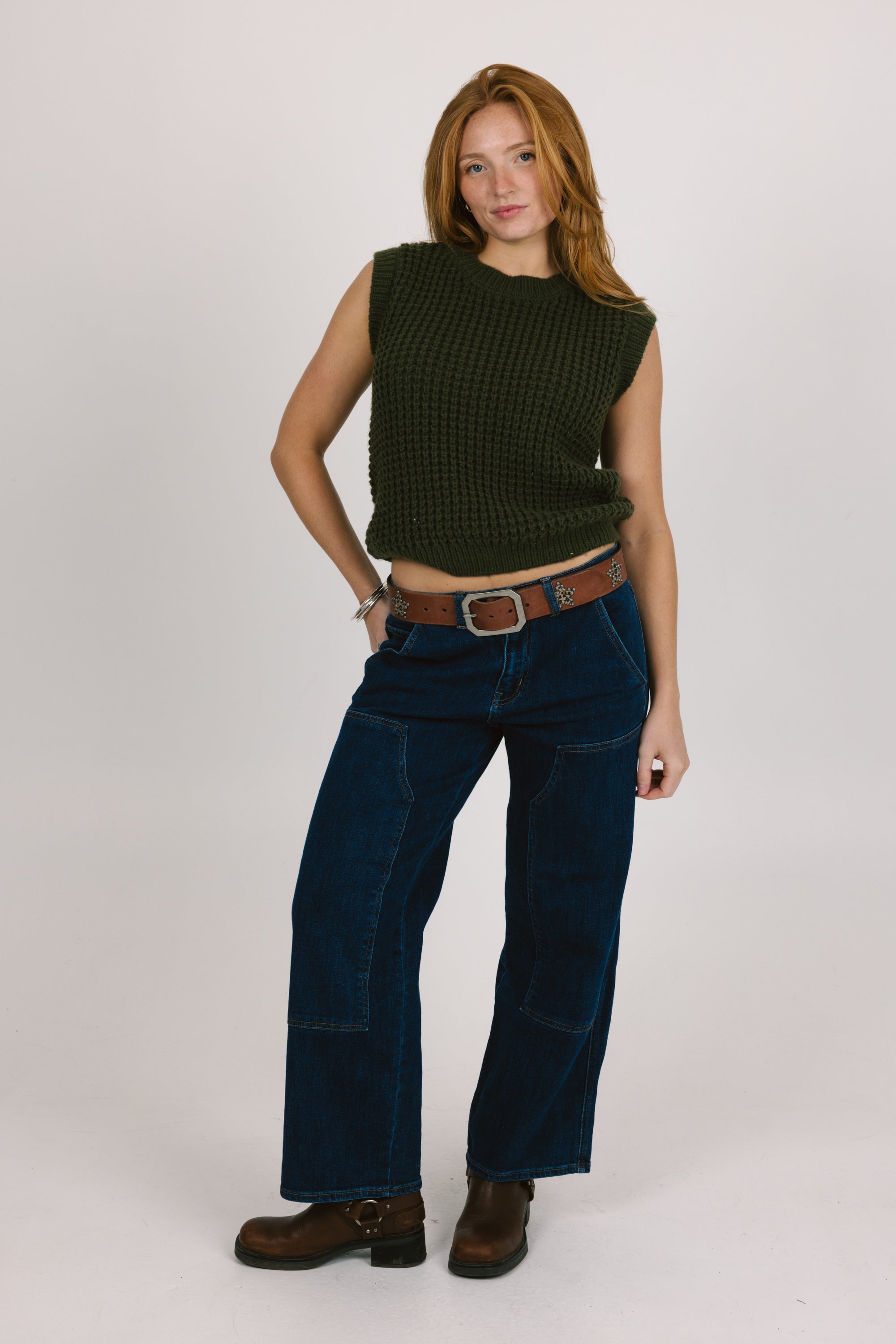 Woman wearing a green sleeveless top and blue jeans on a white background