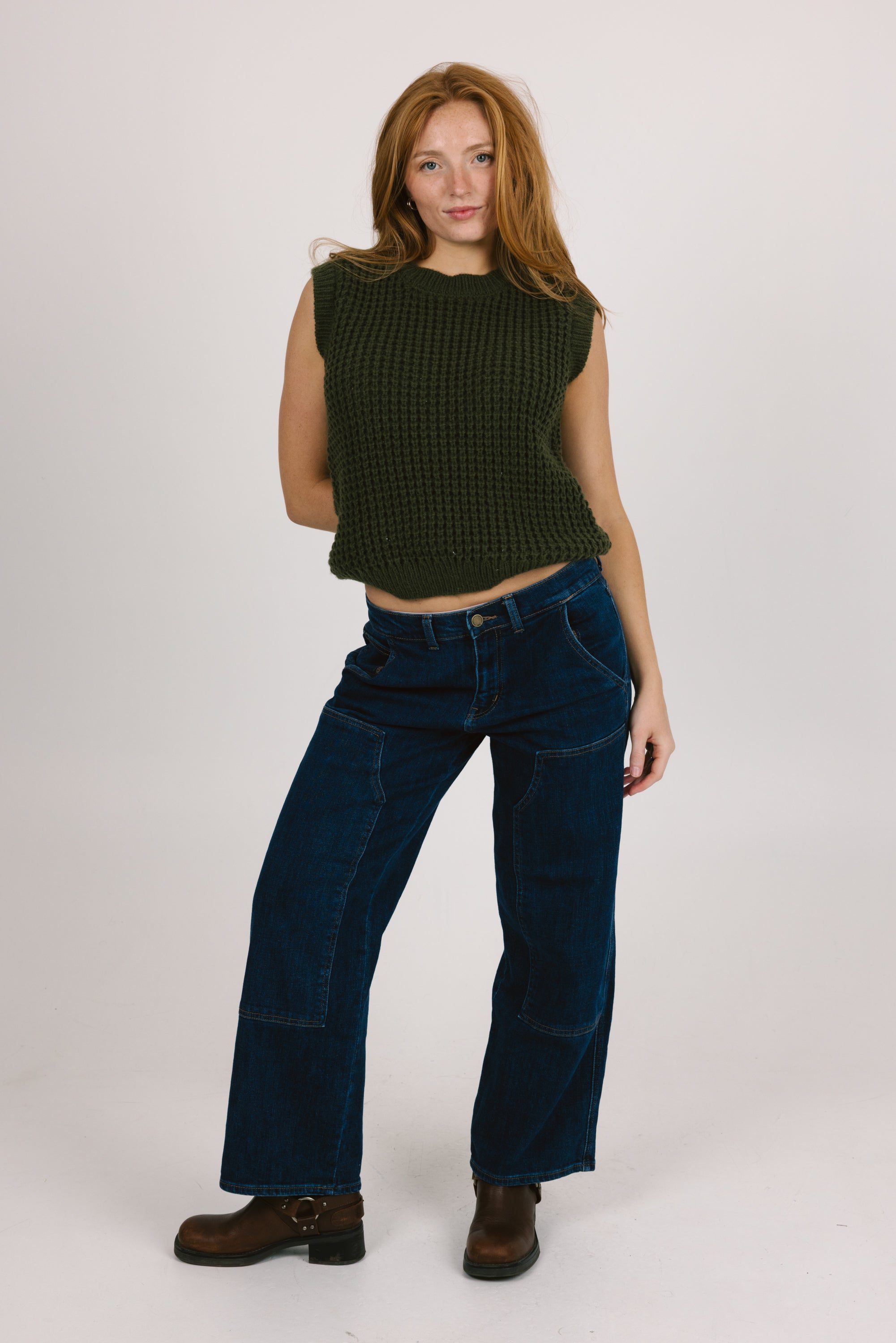 Woman wearing a green sleeveless top and blue jeans on a white background