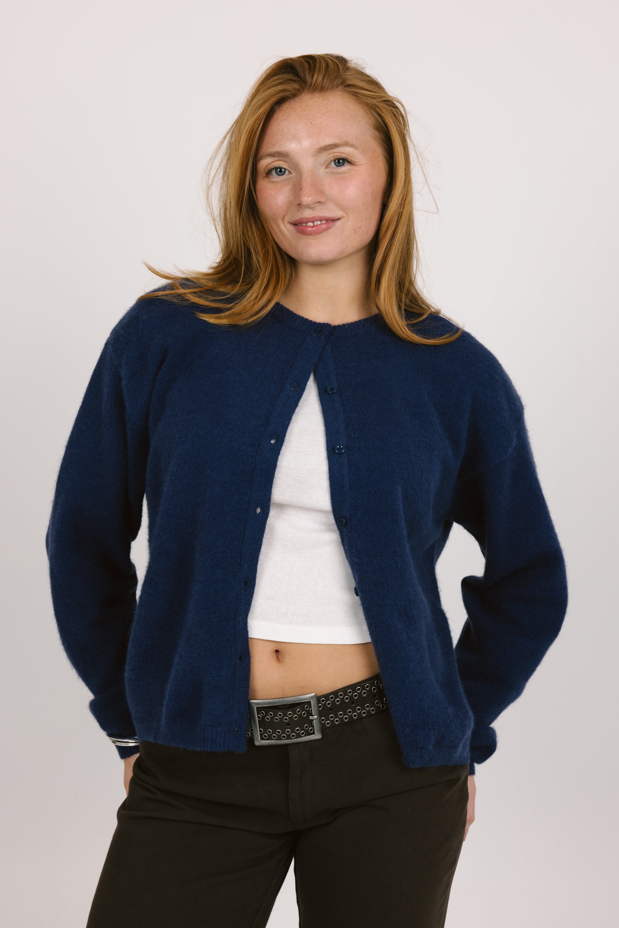 Woman wearing a navy blue cardigan over a white shirt on a plain background