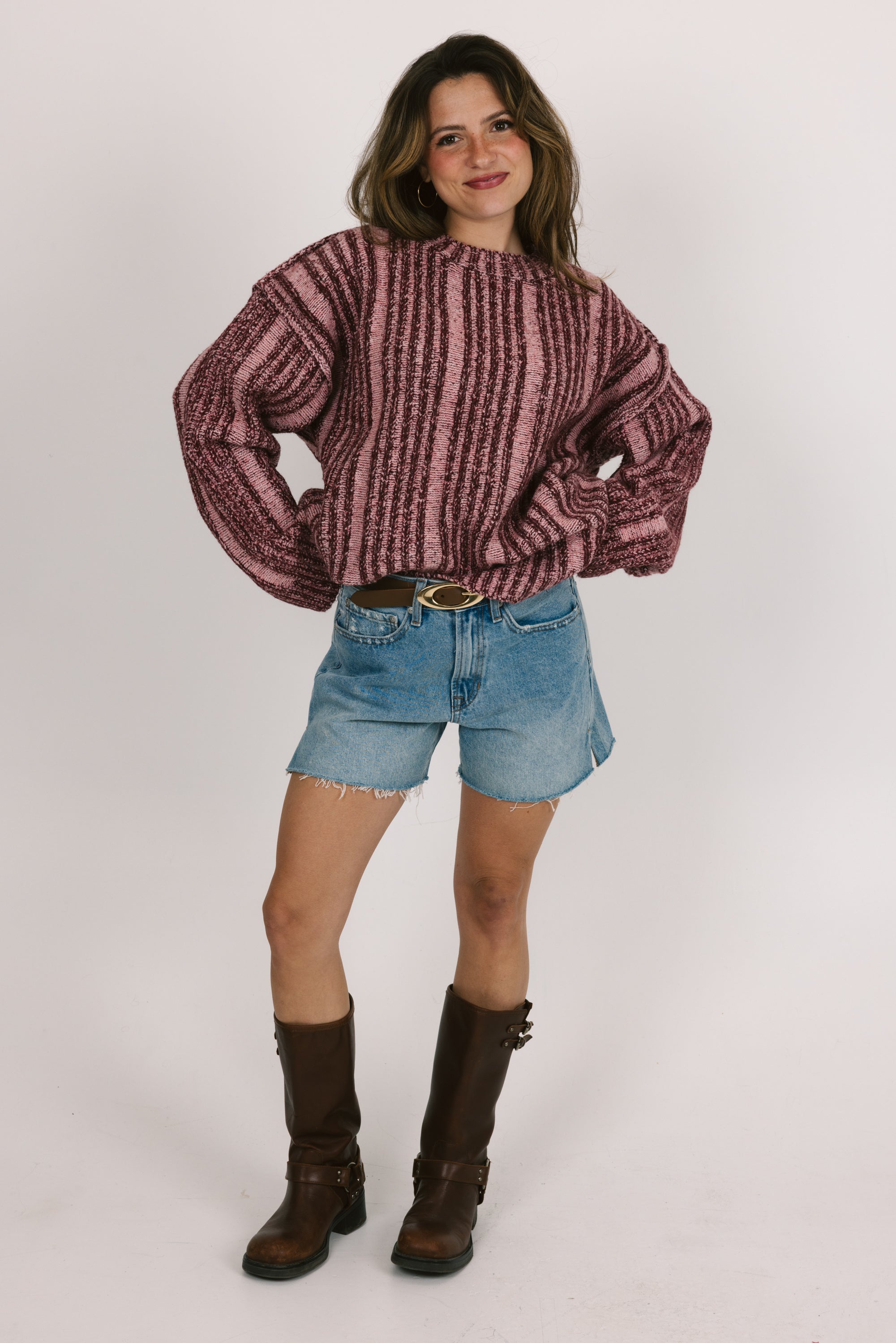 Woman wearing a patterned sweater, denim shorts, and brown boots on a white background