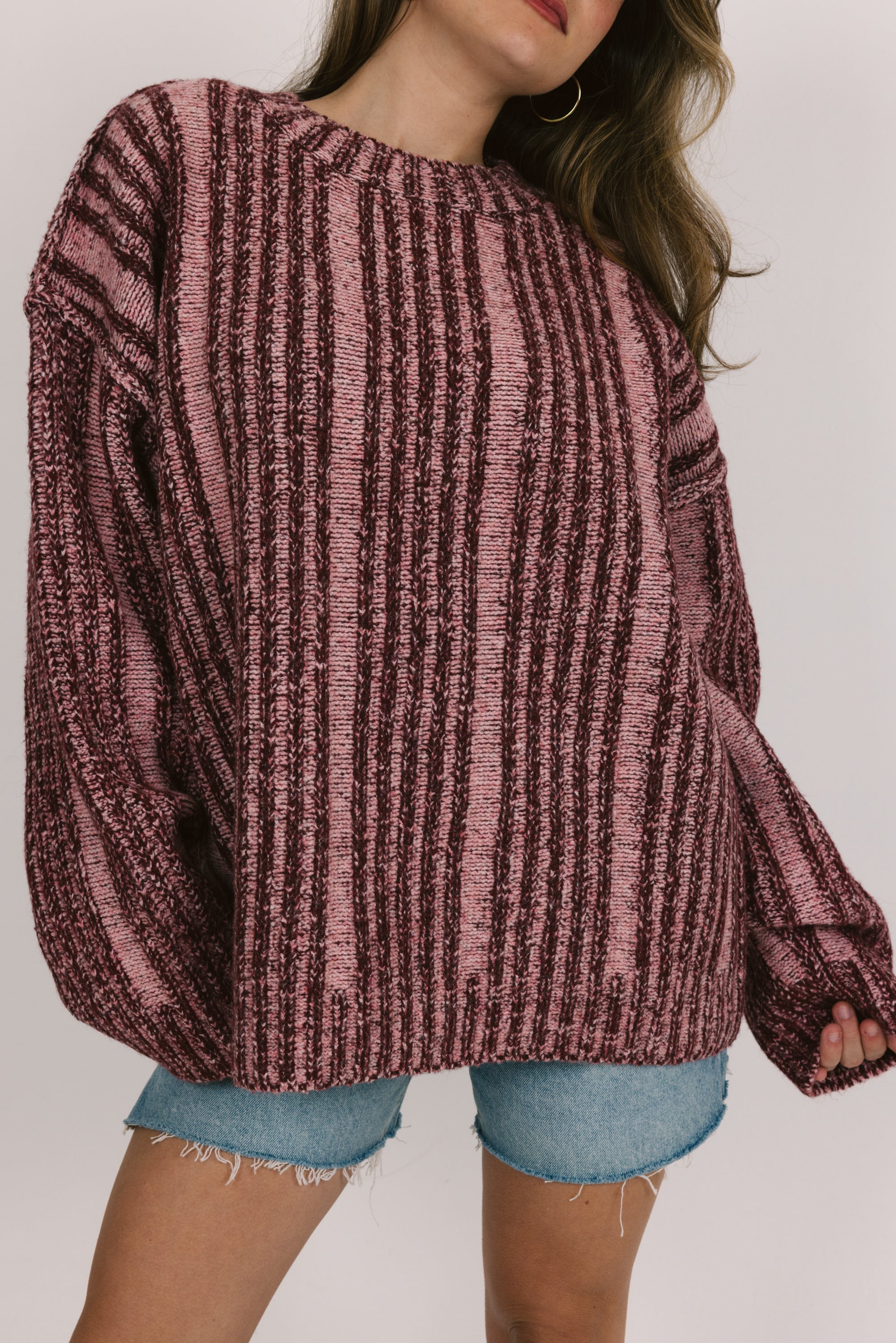 Person wearing a pink knitted sweater and denim shorts on a plain background