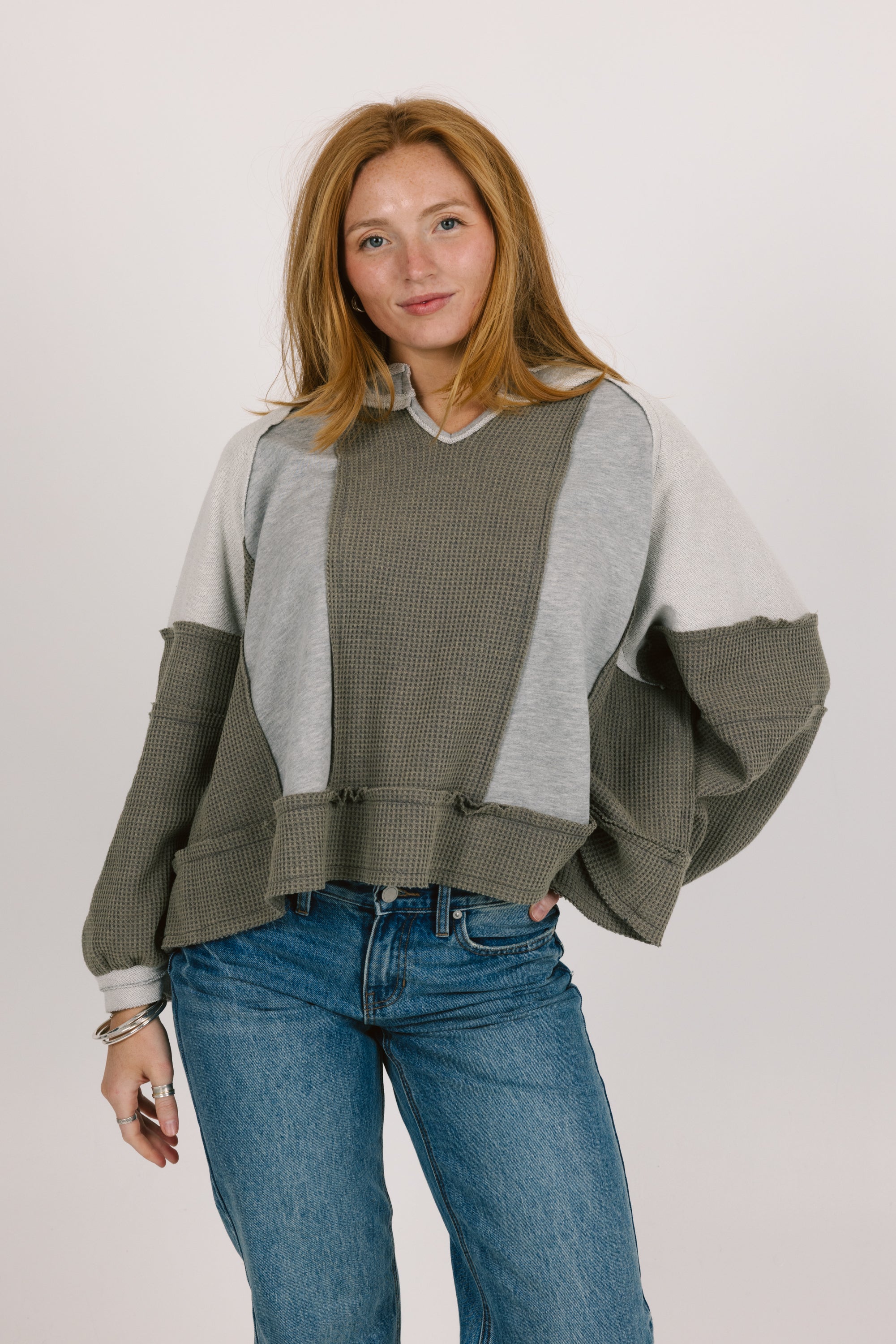 Woman wearing a green and gray sweater with blue jeans on a white background