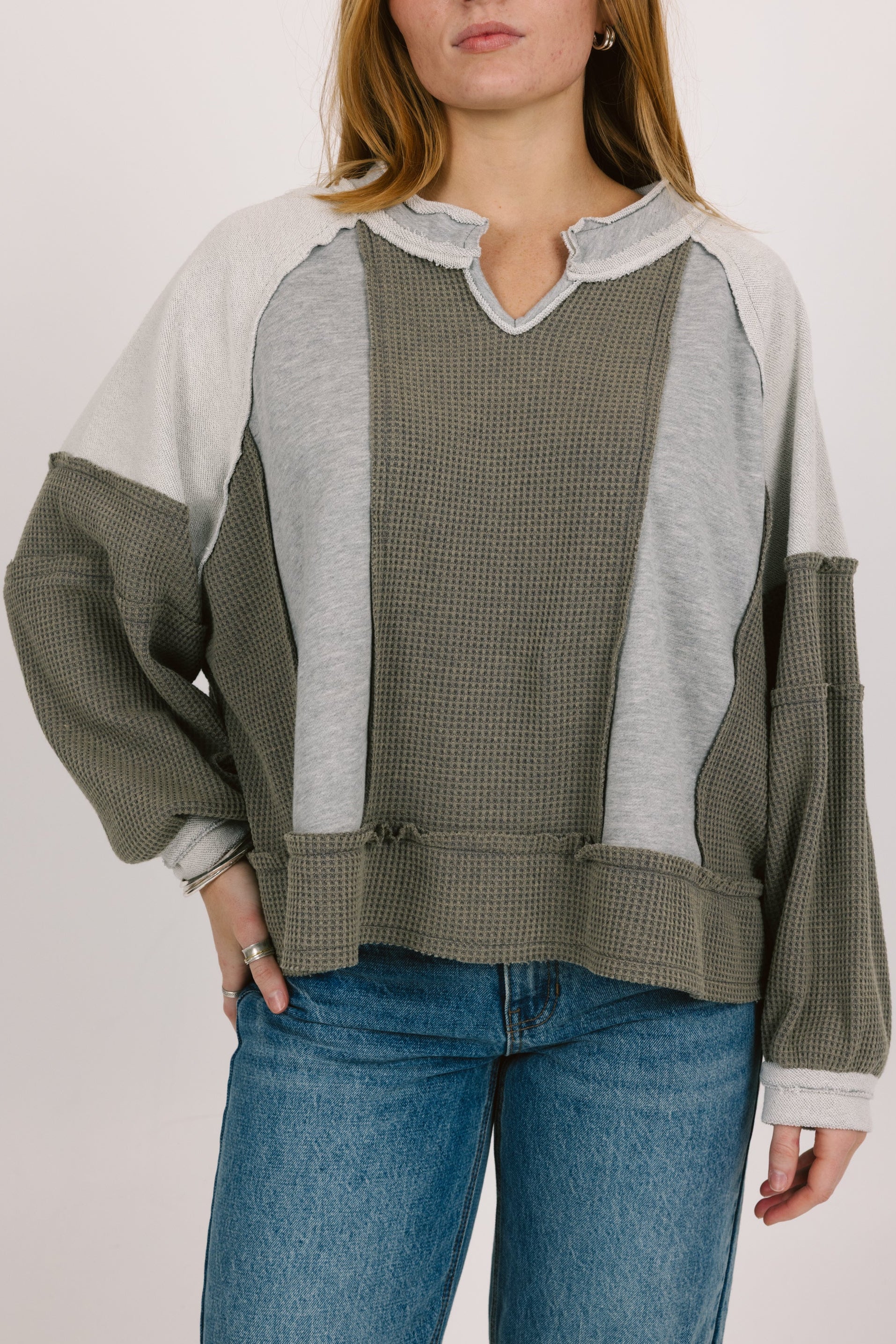 Person wearing a patchwork sweater with green, gray, and white sections on a plain background