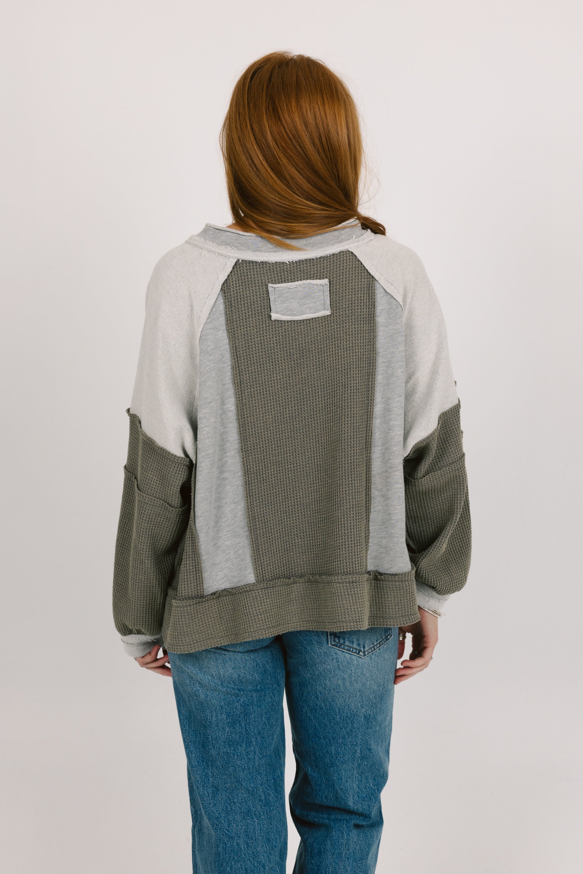 Person wearing a gray and green sweater with a plain background