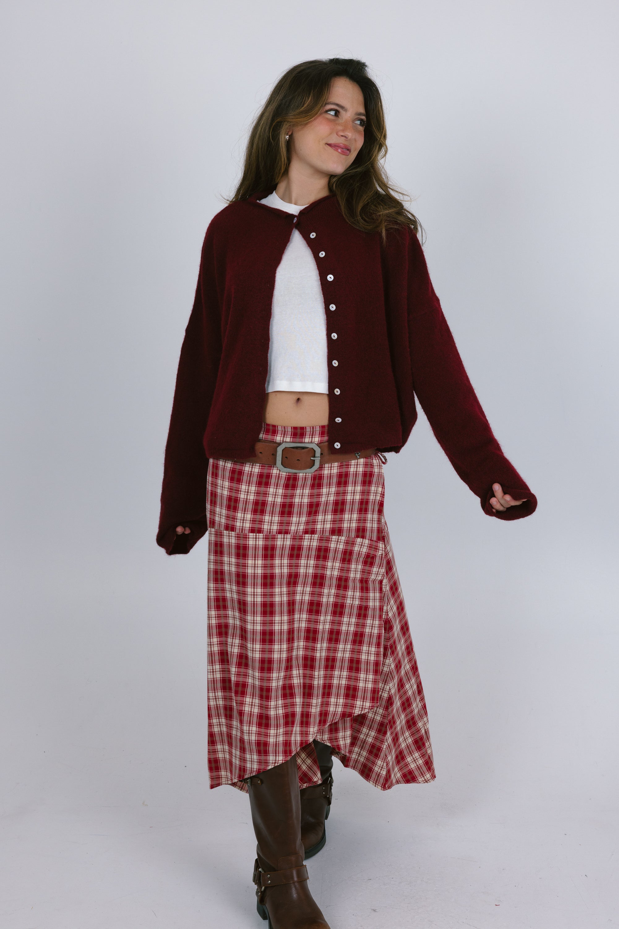 Woman wearing a burgundy cardigan, white shirt, red plaid skirt, and brown boots on a white background