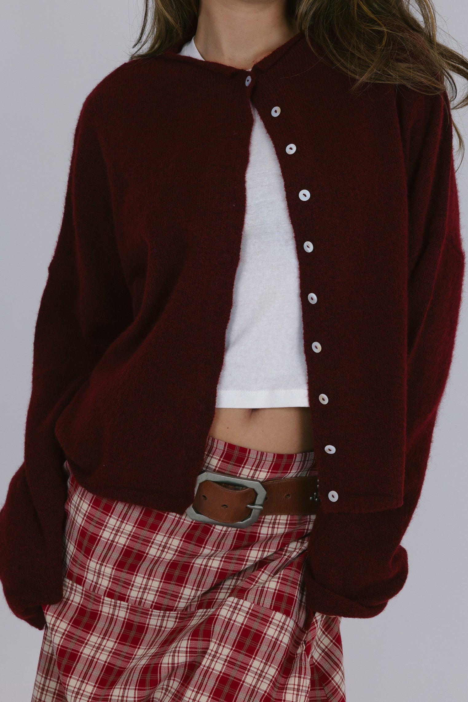 Person wearing a maroon varsity jacket over a white shirt and red plaid pants on a plain background