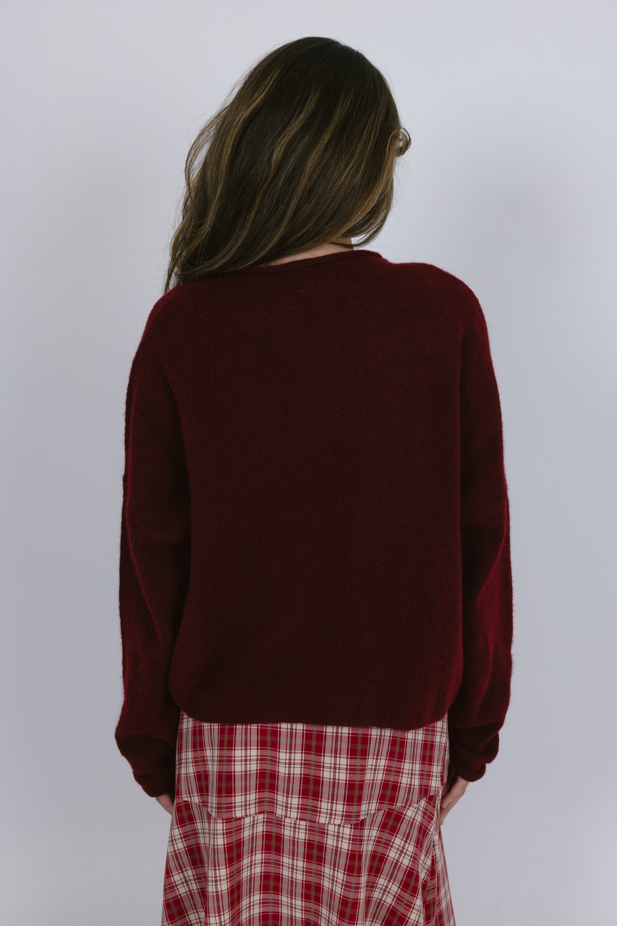 Person wearing a burgundy sweater and plaid pants against a white background