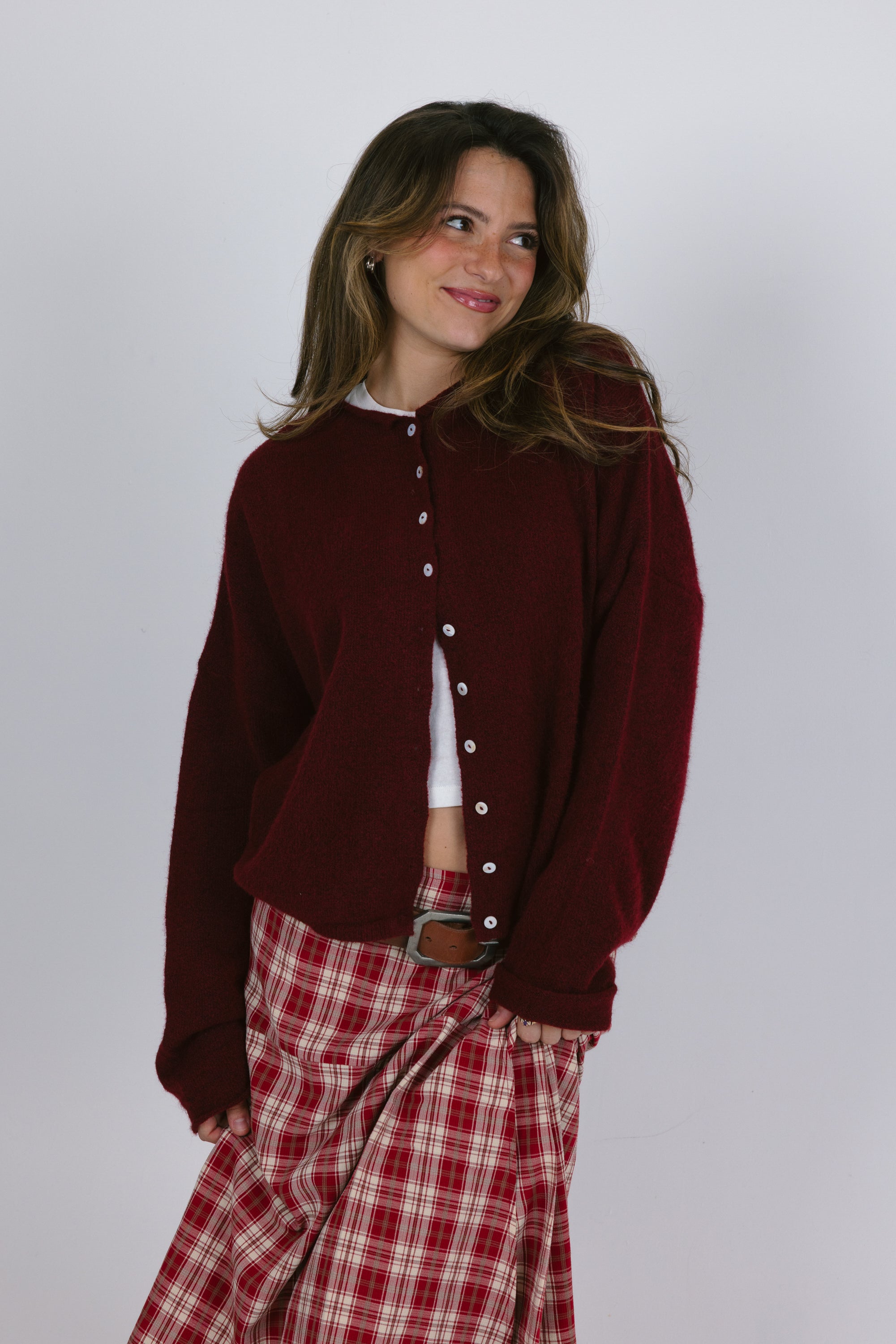 Woman wearing a burgundy cardigan over a white shirt with red plaid pants on a plain background