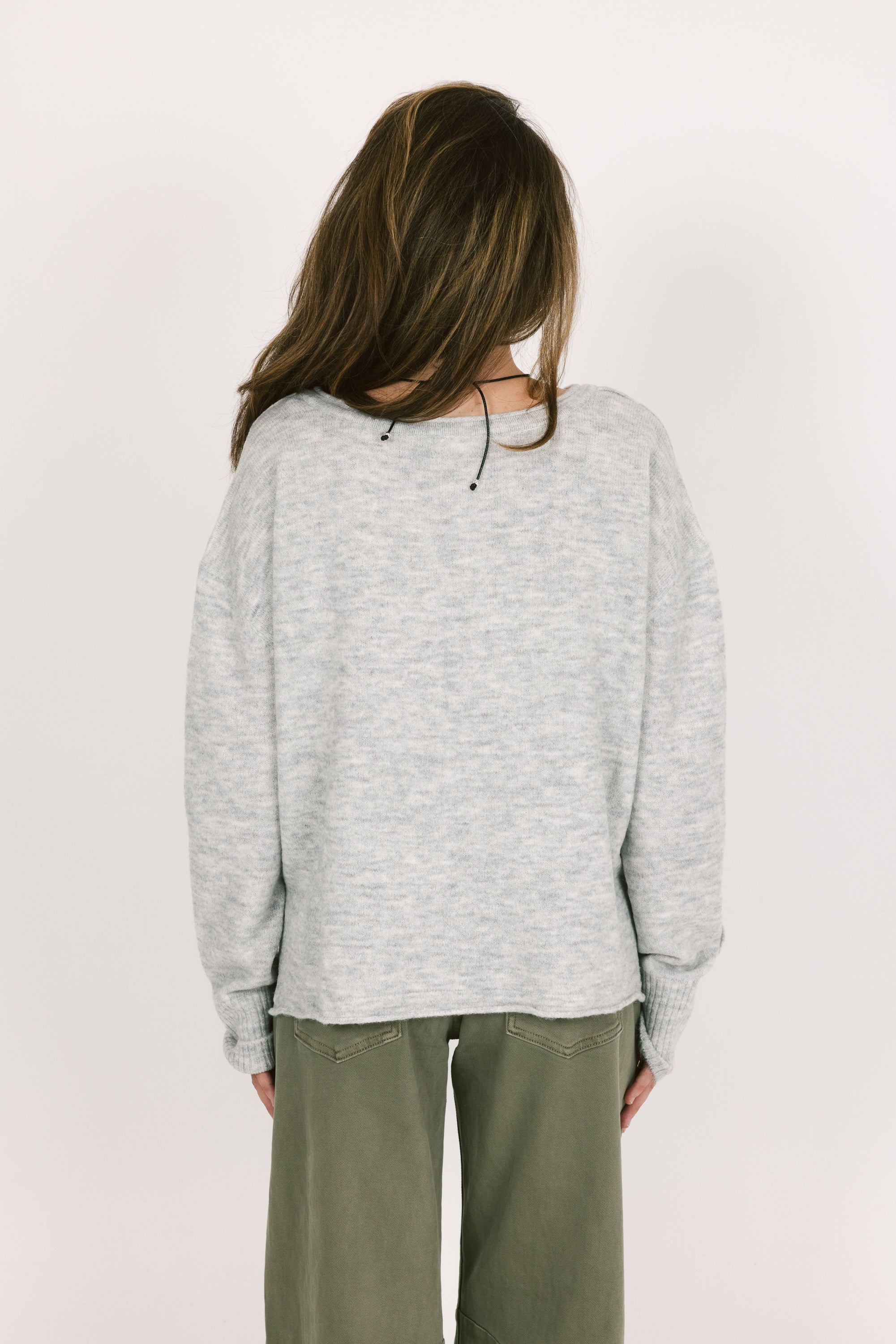 Person wearing a light gray sweater and green pants on a white background