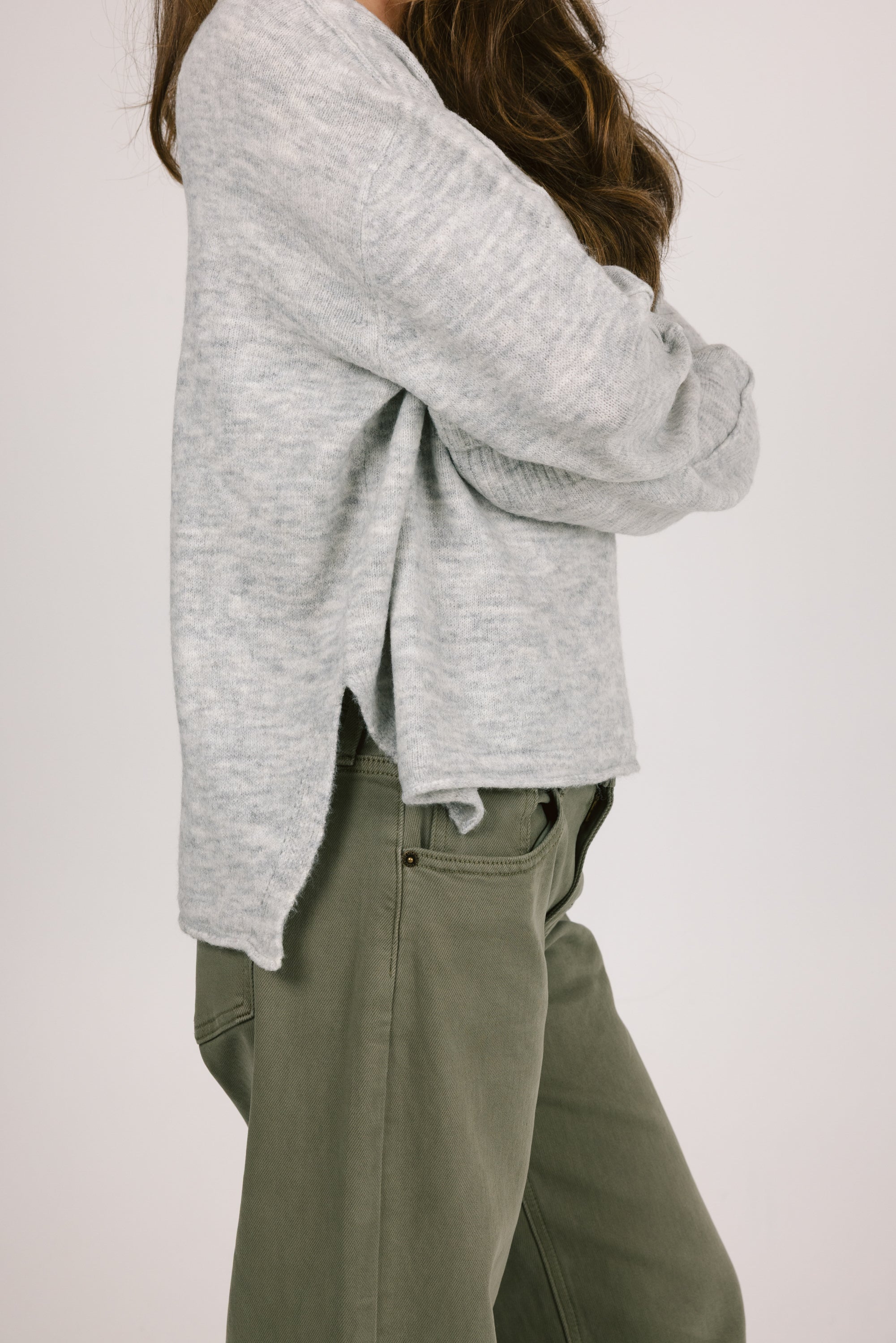 Person wearing a gray sweater and green pants on a white background