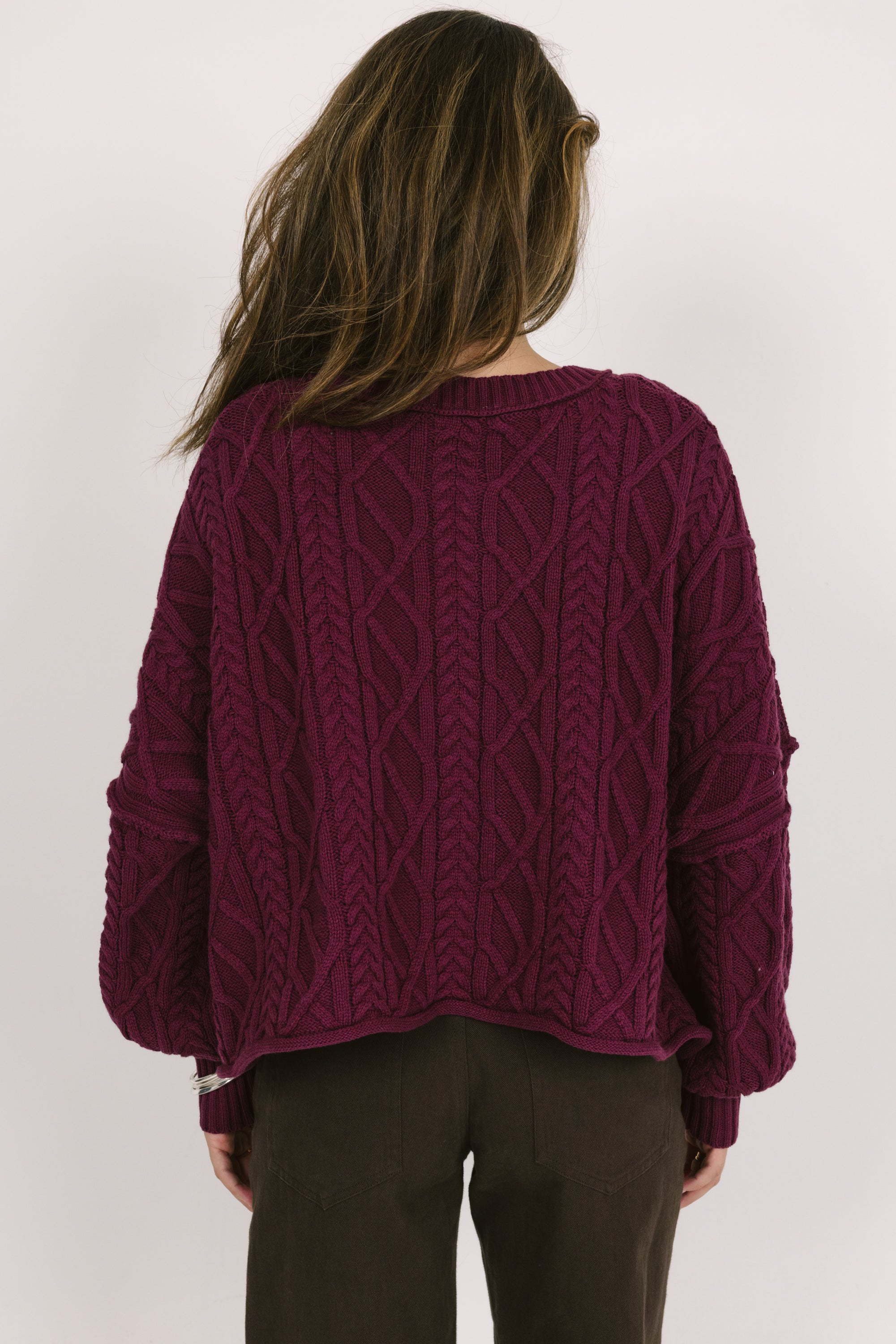 Person wearing a purple cable knit sweater on a white background