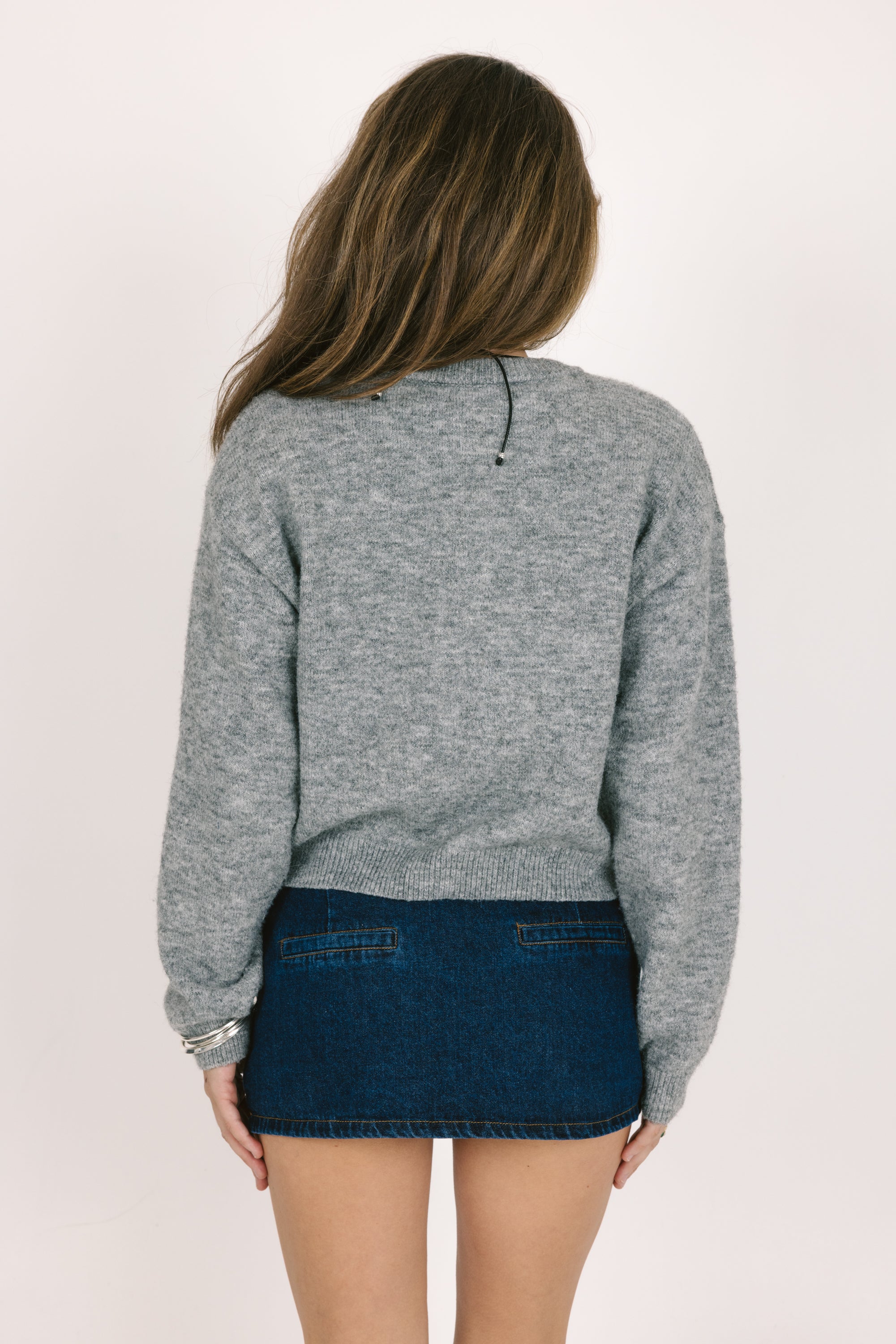 Person wearing a gray sweater and blue denim skirt on a plain background